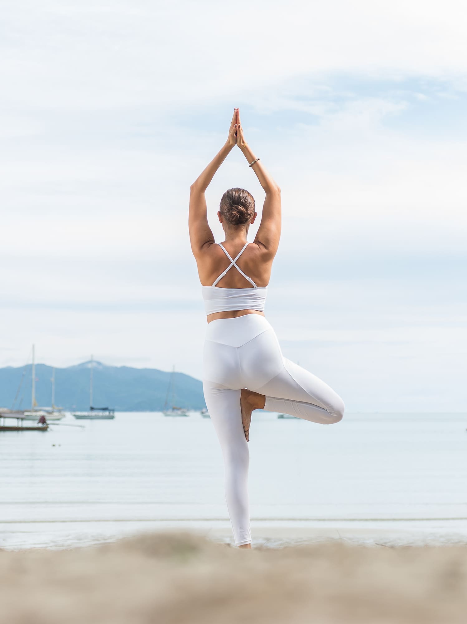 a woman standing on one leg on a beach with her arms raised