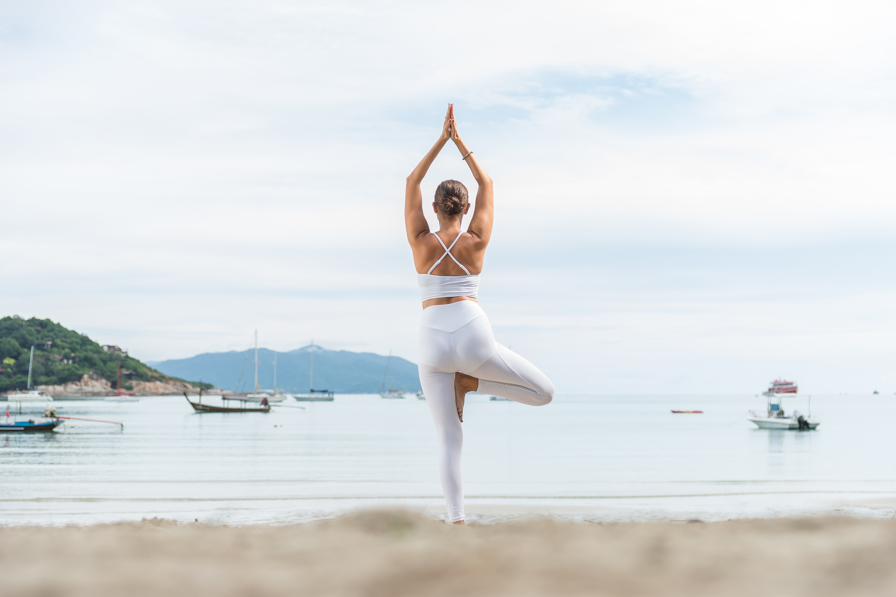 Woman in white yoga wear doing tree pose on a tropical beach.