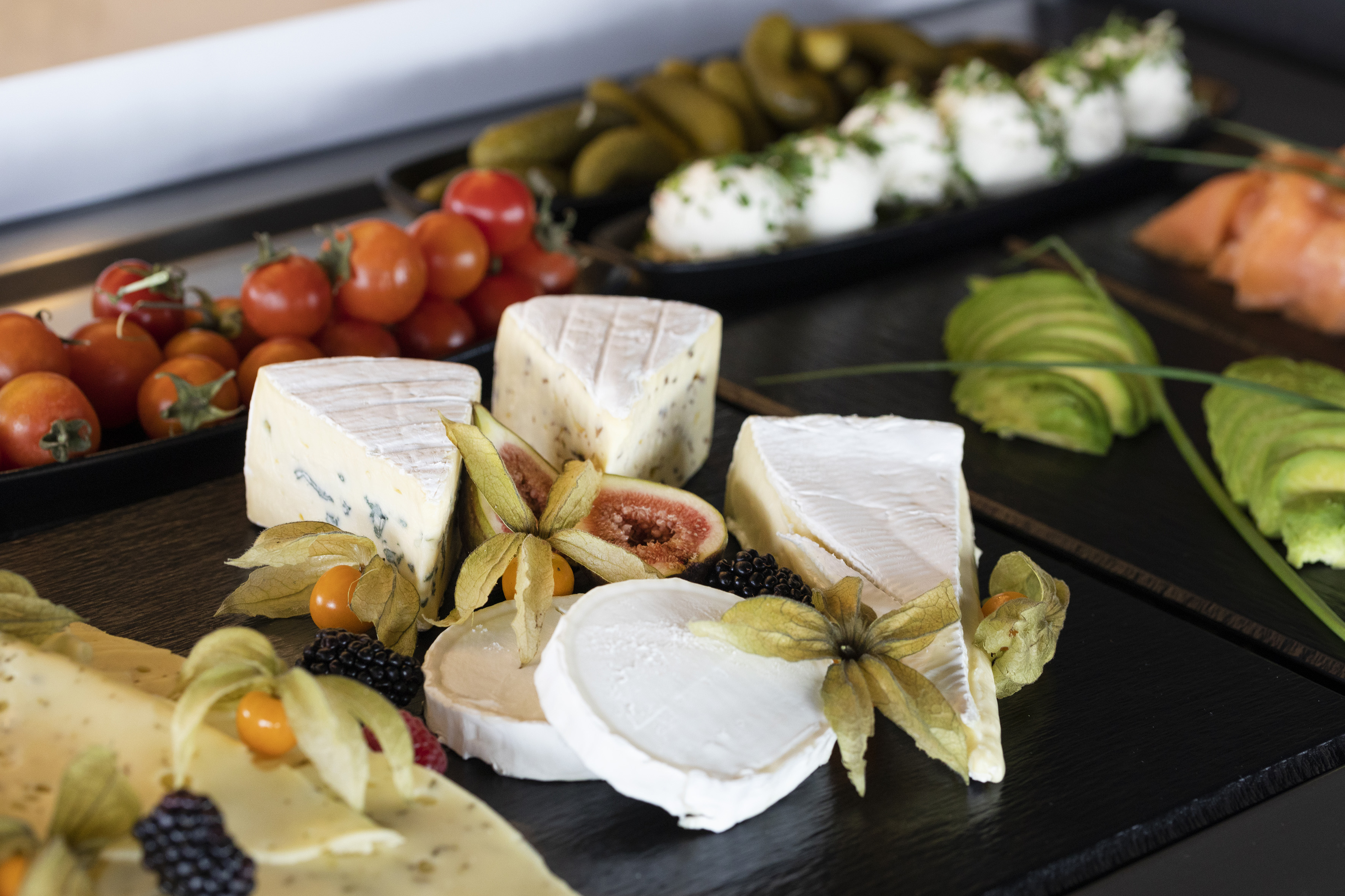 Gourmet cheese board with brie, blue cheese, figs, berries, tomatoes, and avocado.