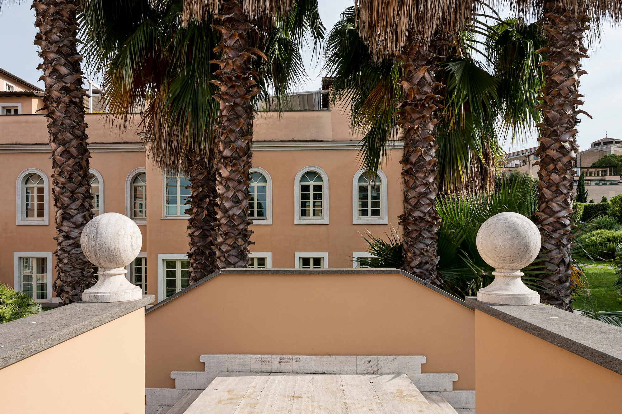 Tan building with arched windows, flanked by tall palm trees and stone finials.