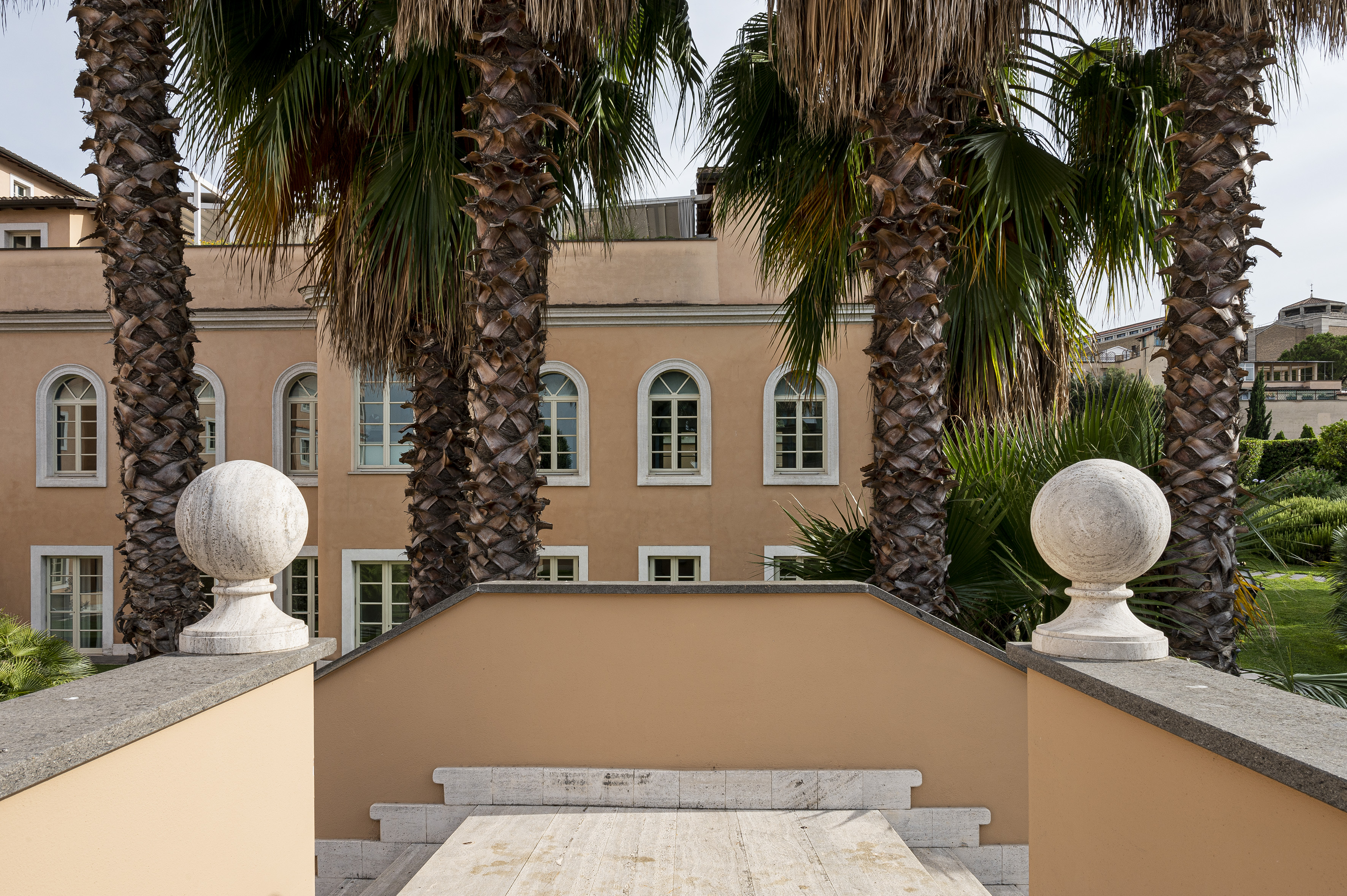 Tan building with arched windows, flanked by tall palm trees and stone finials.