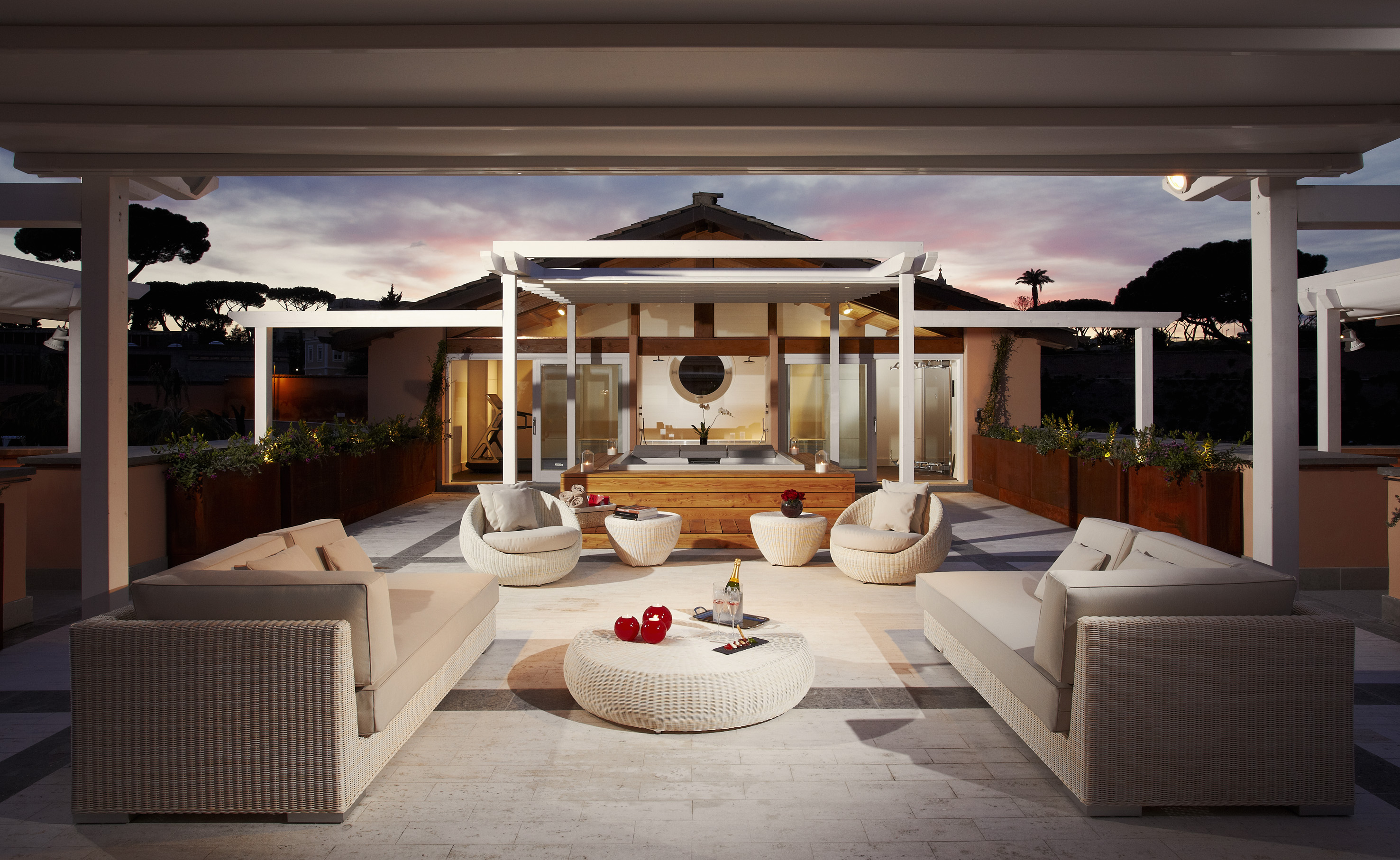 Luxury outdoor patio with wicker lounge furniture, modern pergola, and spa at sunset.