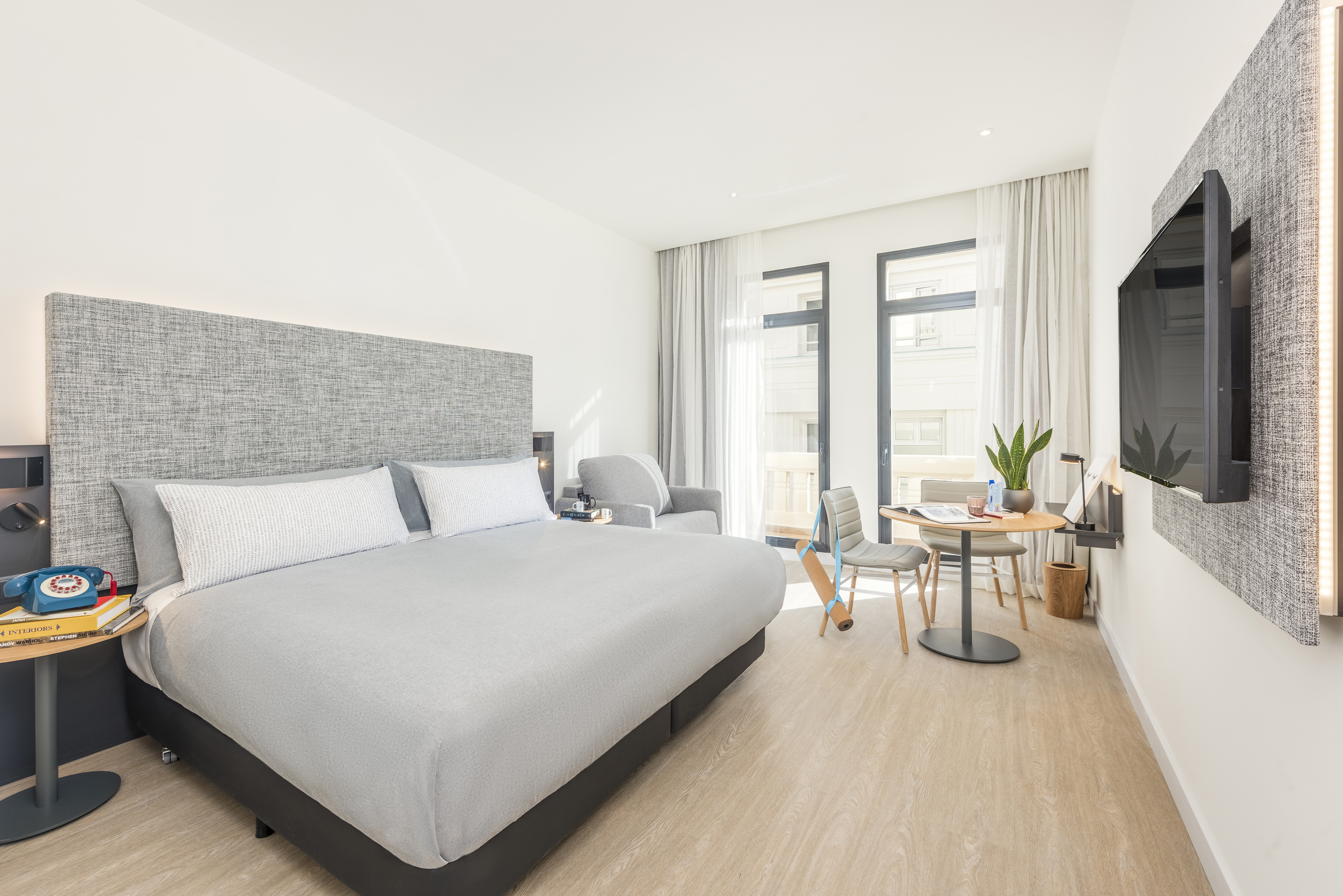 Modern hotel room with comfortable bed, small dining area, and balcony access.