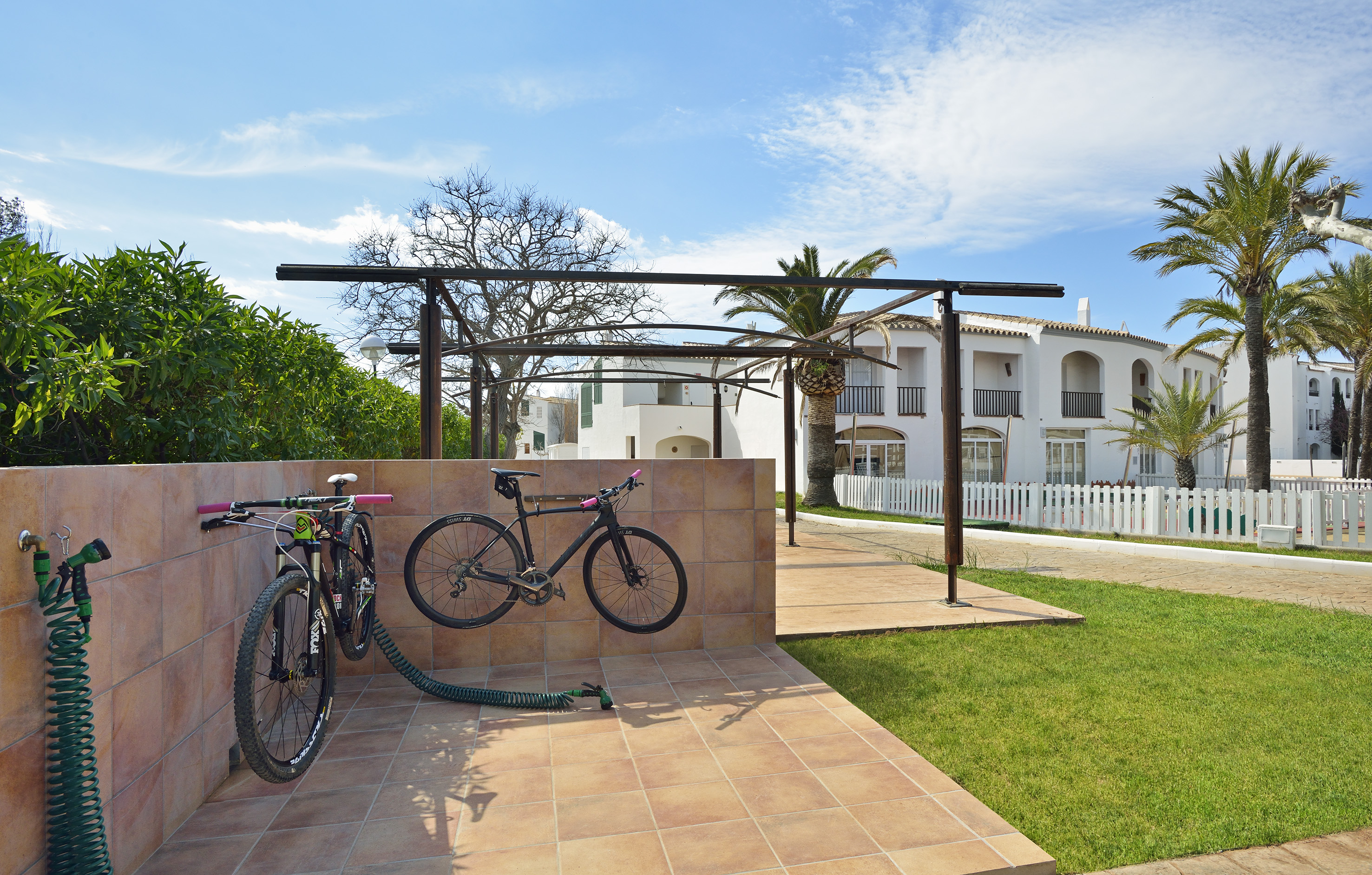 Bike wash station with two bicycles, hose, palm trees, and resort villas.