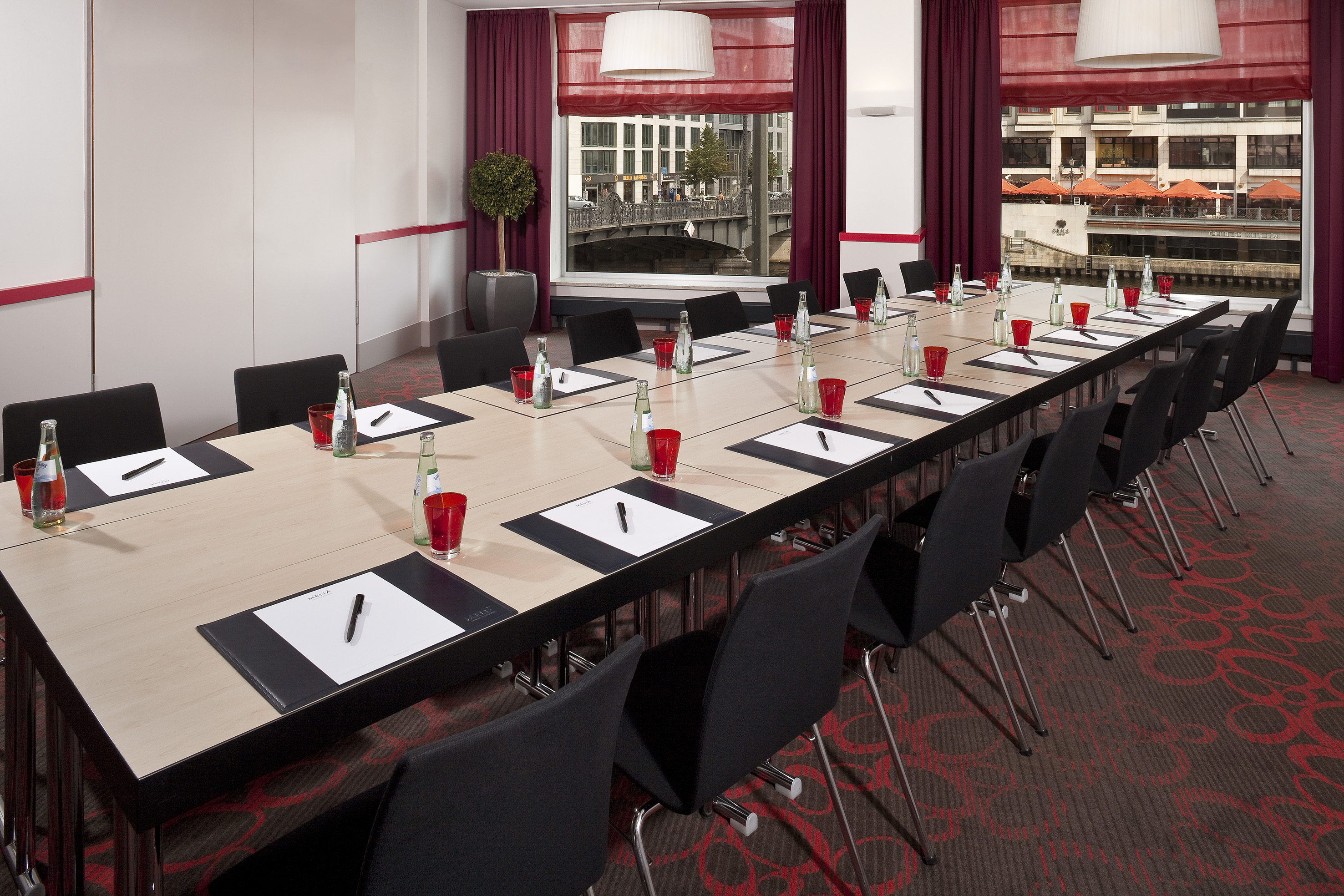U-shaped meeting room with city view, black chairs, red accents, and place settings.
