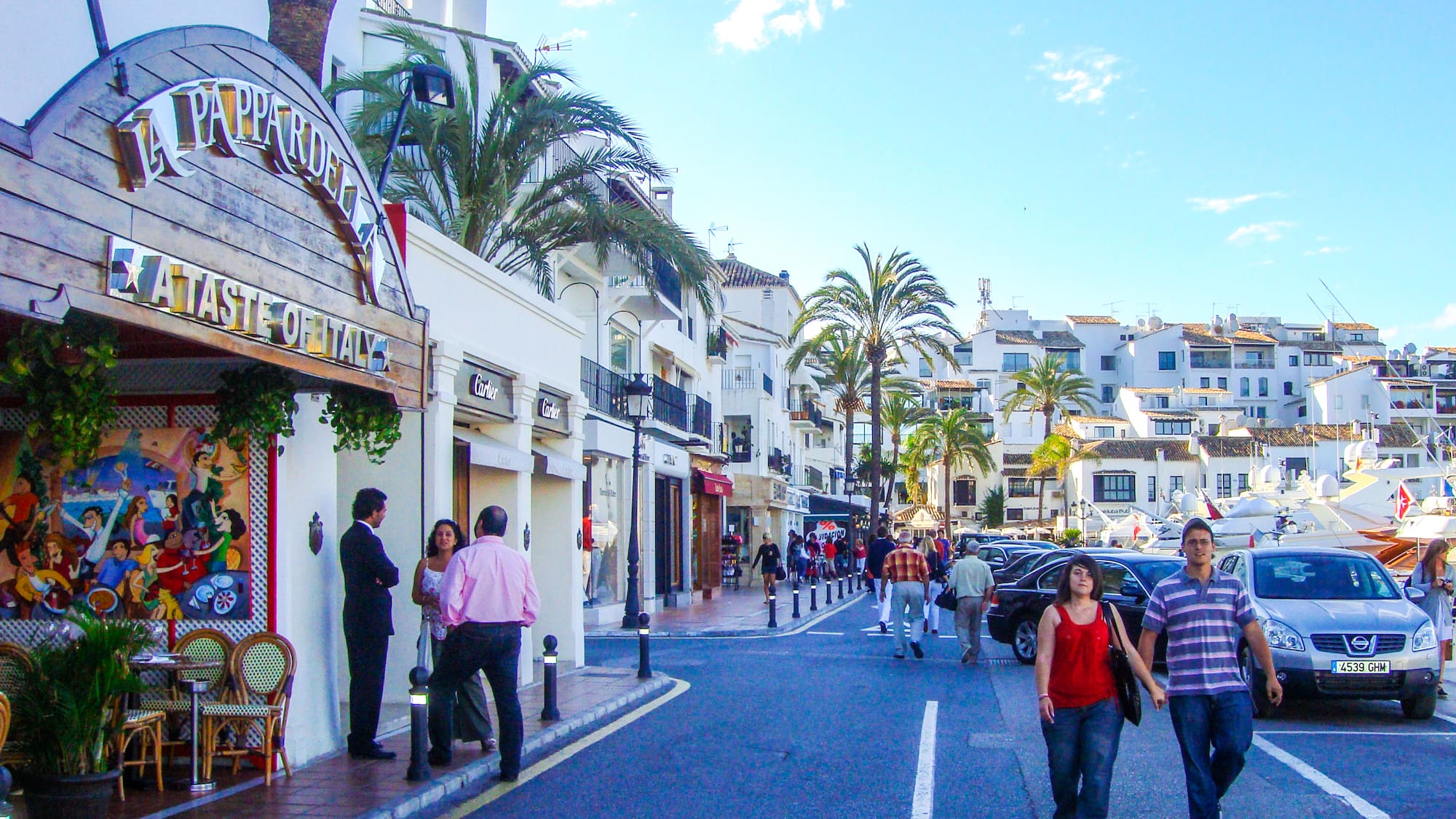 people walking on a street with buildings and palm trees