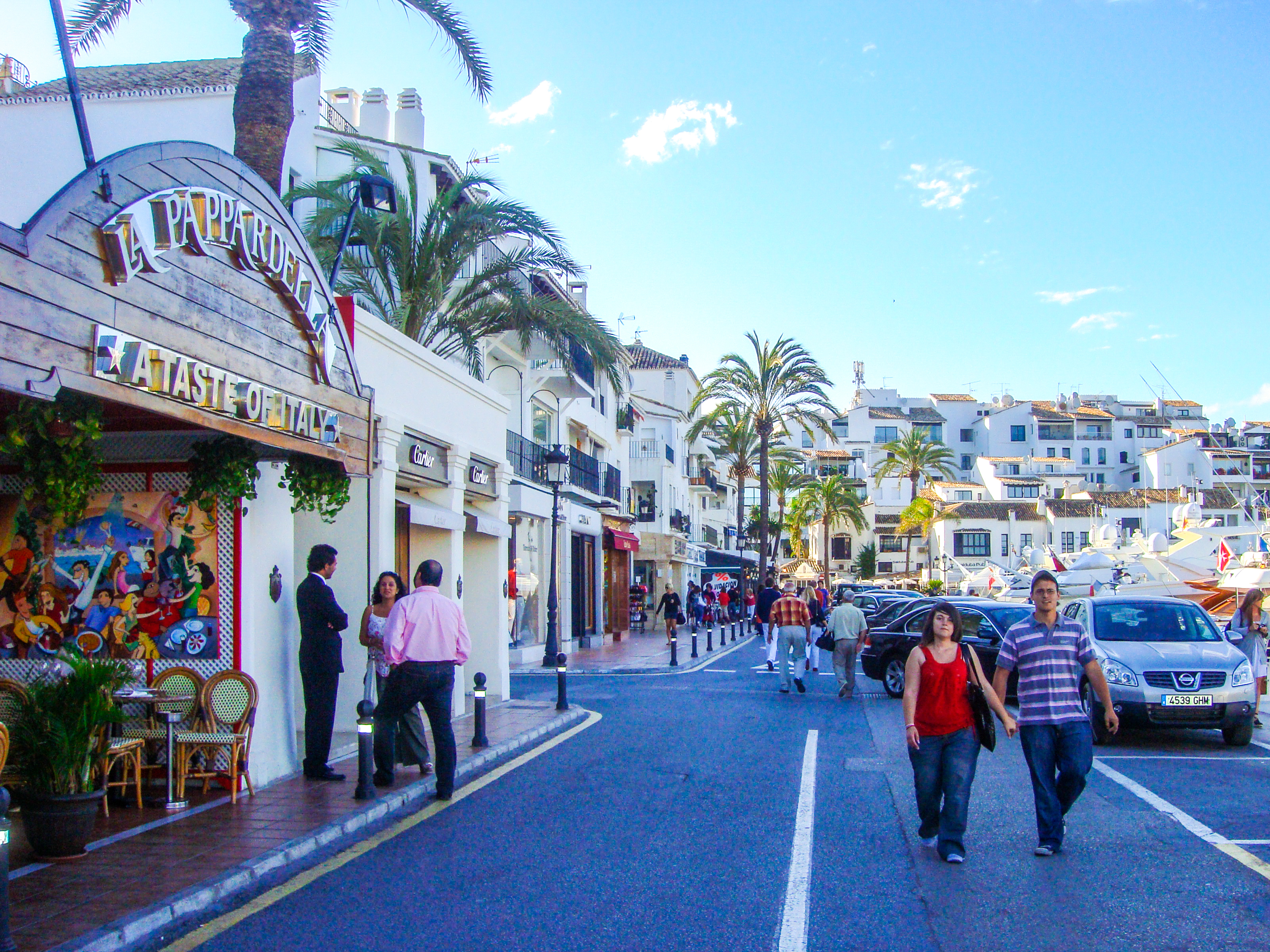 people walking on a street with buildings and palm trees