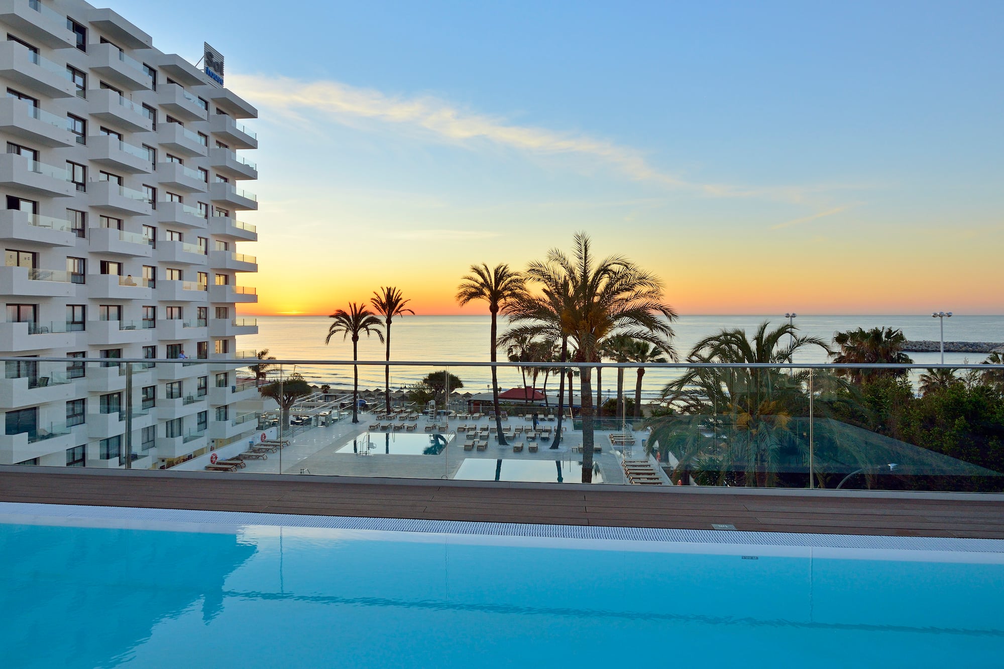 a pool with palm trees and a building with a body of water in the background