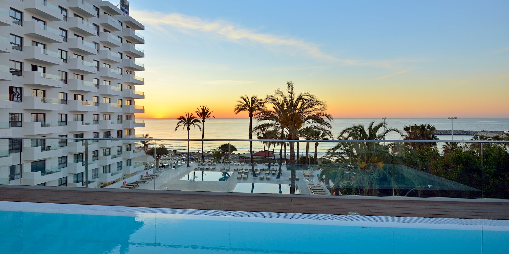 a pool with palm trees and a building with a body of water in the background