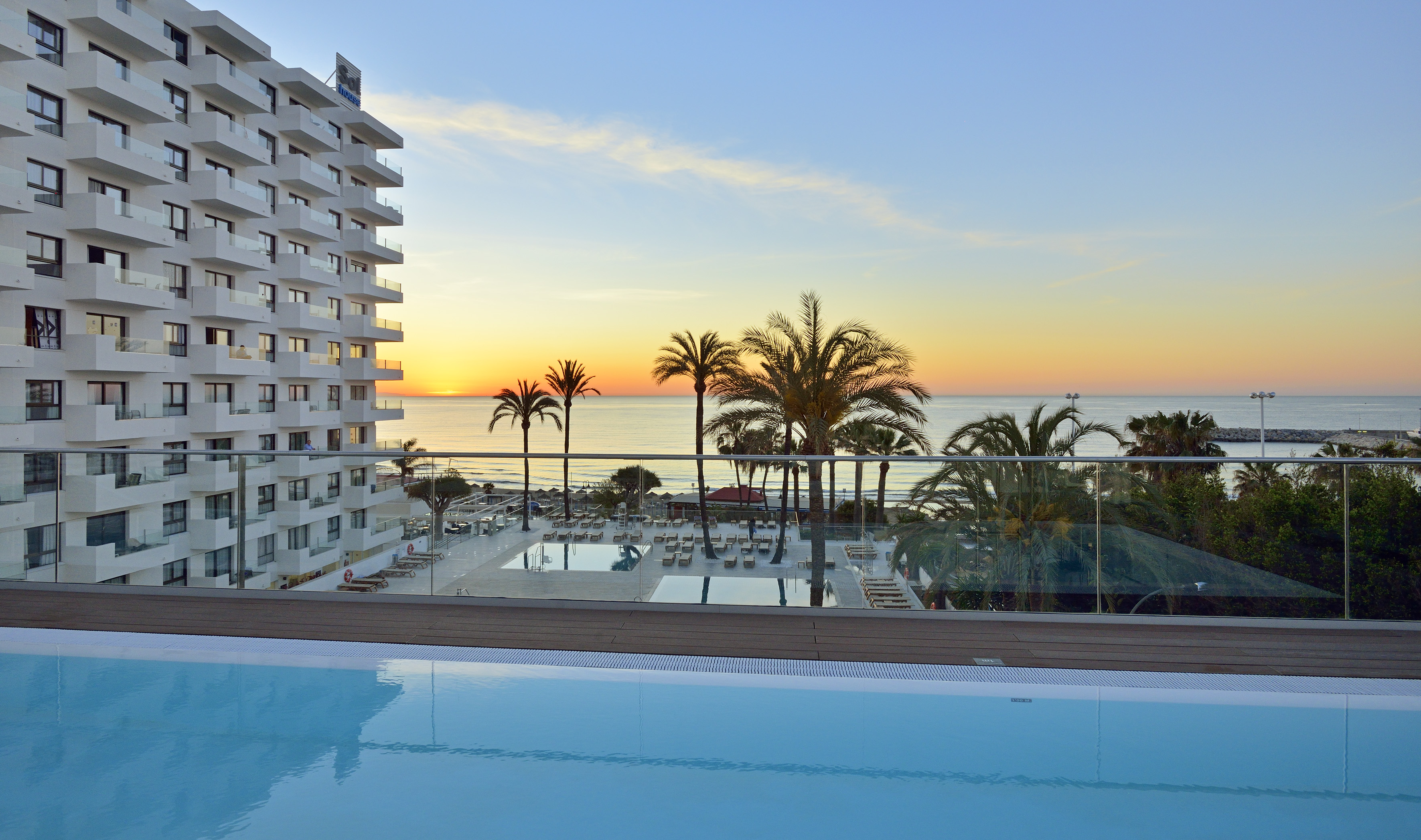 a pool with palm trees and a building with a body of water in the background