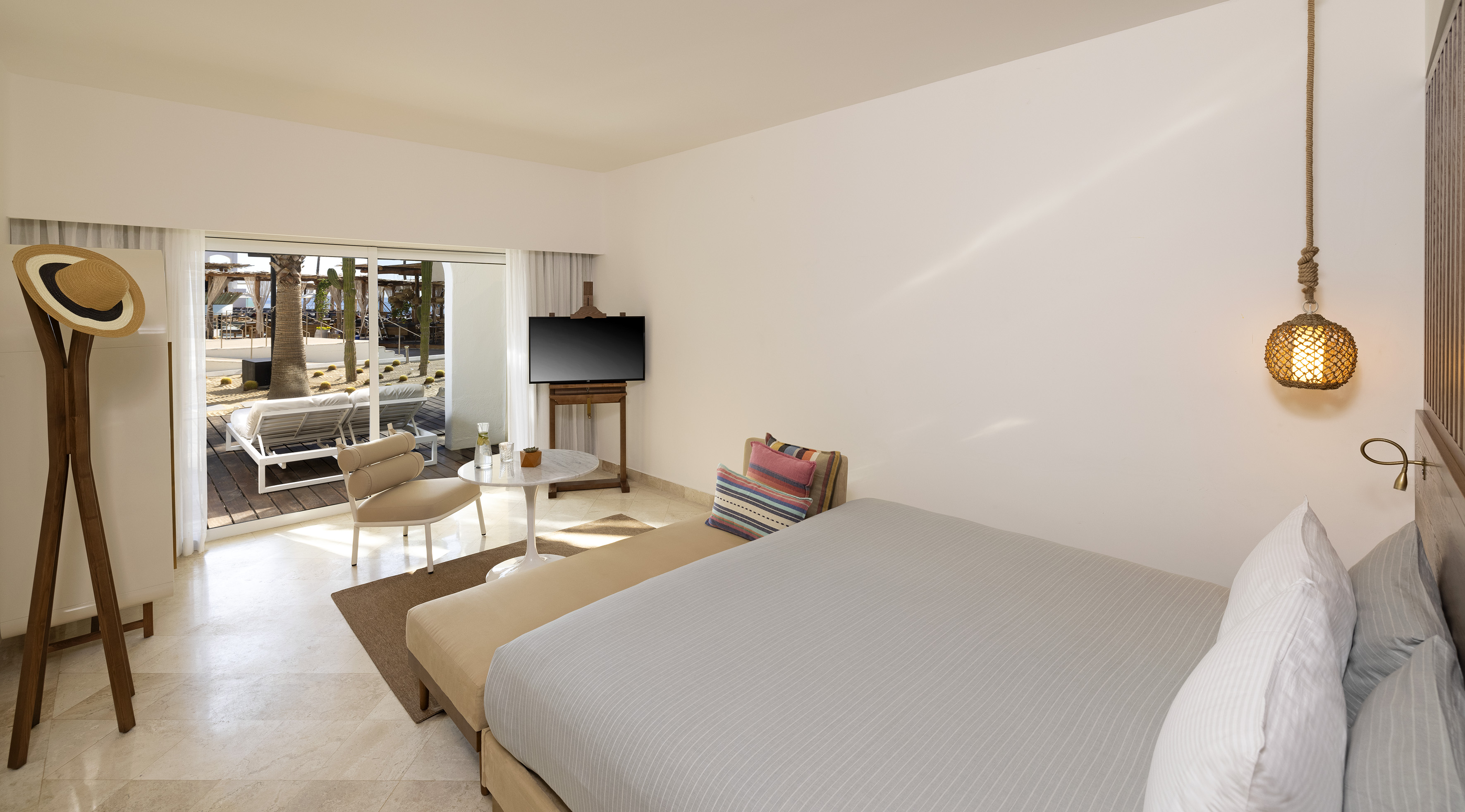 Modern resort bedroom with patio, loungers, palm trees, and TV.