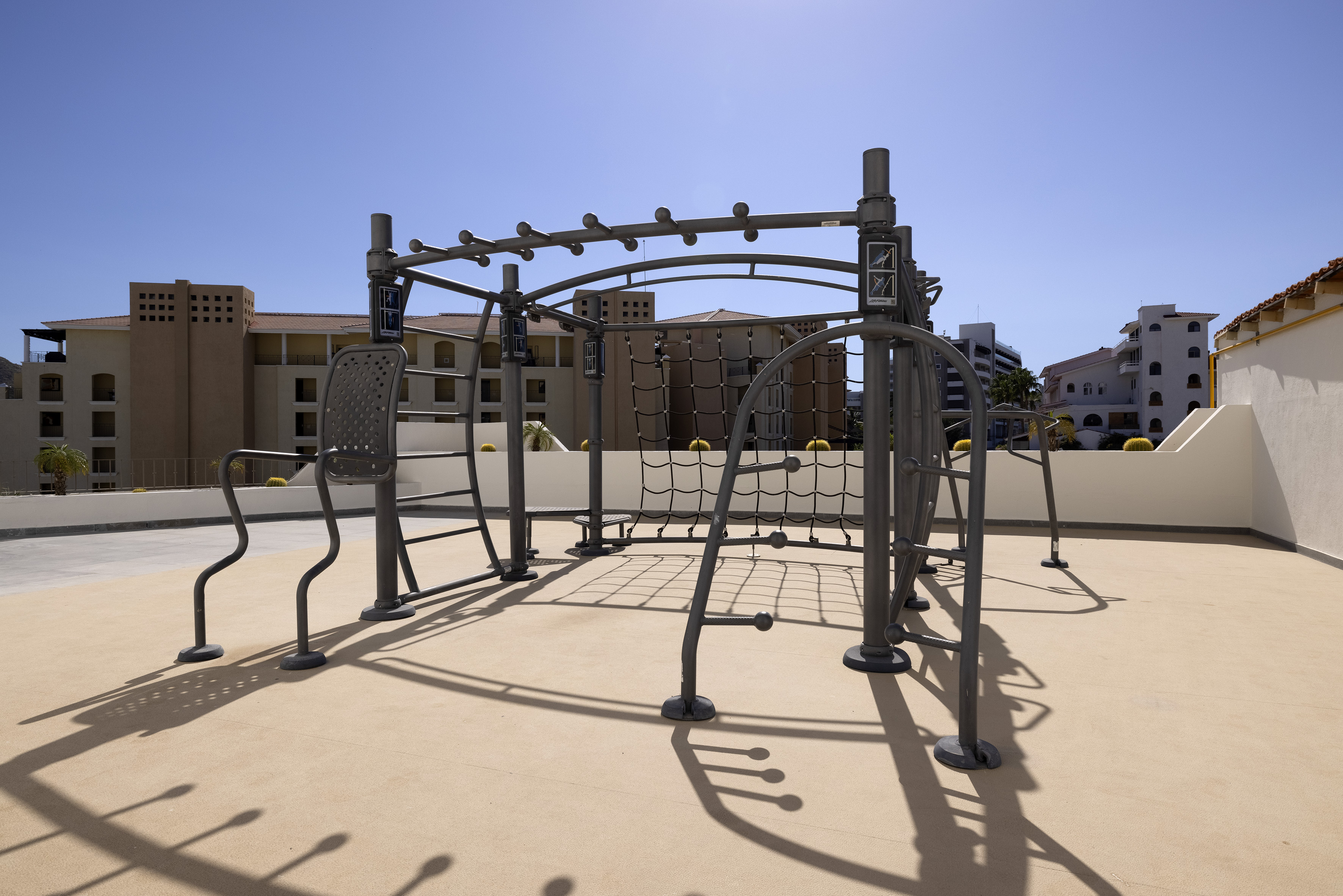 Outdoor calisthenics gym with monkey bars and climbing net on a sunny patio.