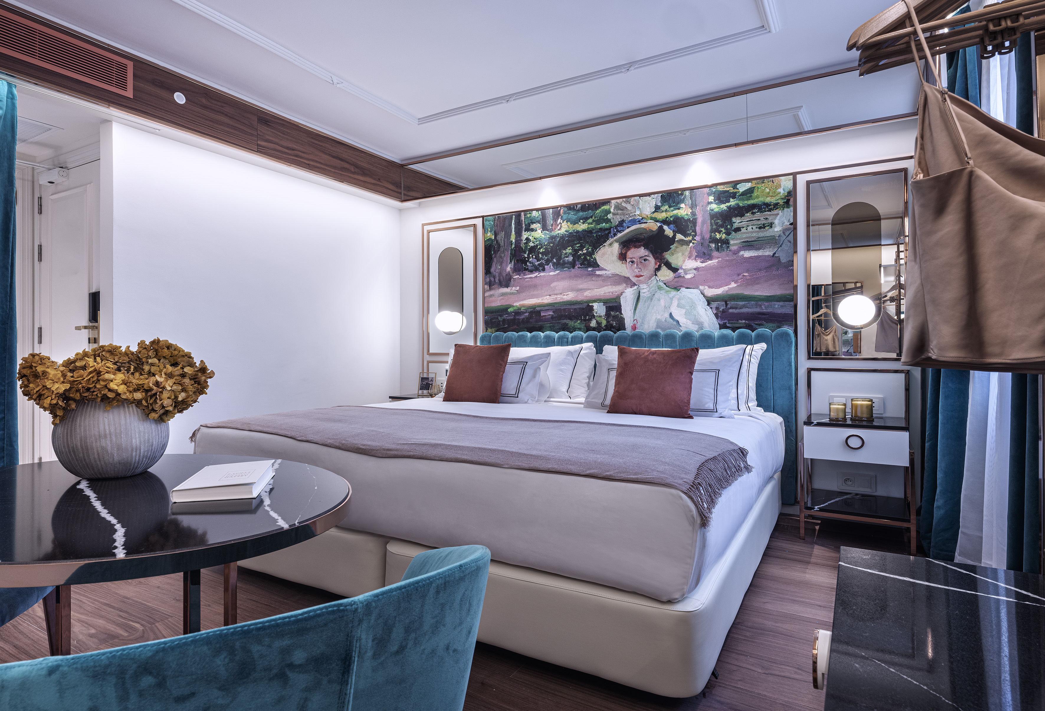 Luxury hotel room with plush bed, blue velvet headboard, and elegant wall art.