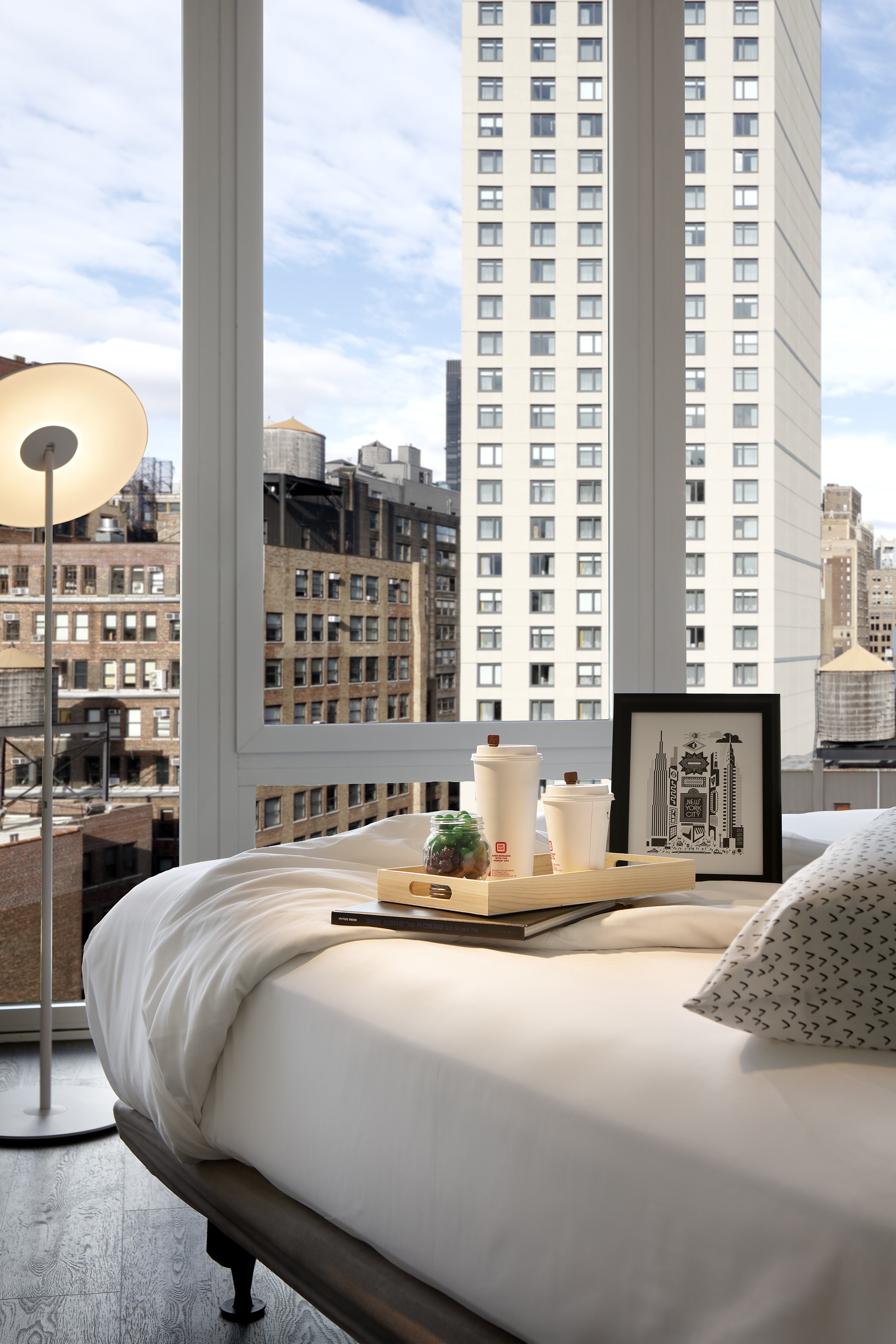Modern hotel room bed with breakfast tray and NYC cityscape window view.