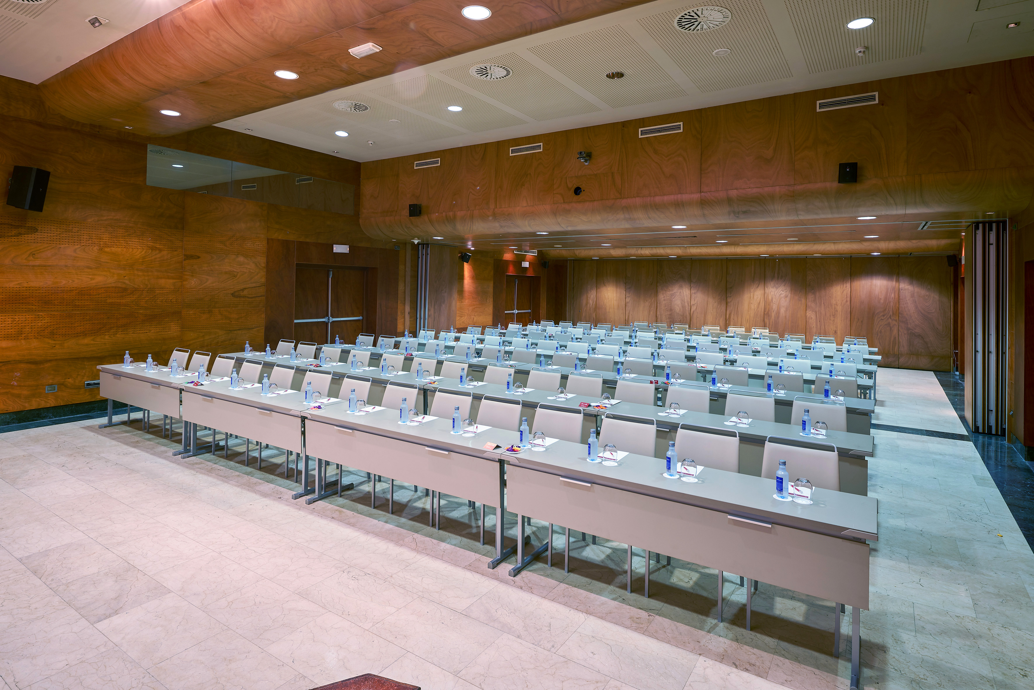 Modern conference room: wood walls, rows of tables & chairs ready for event.