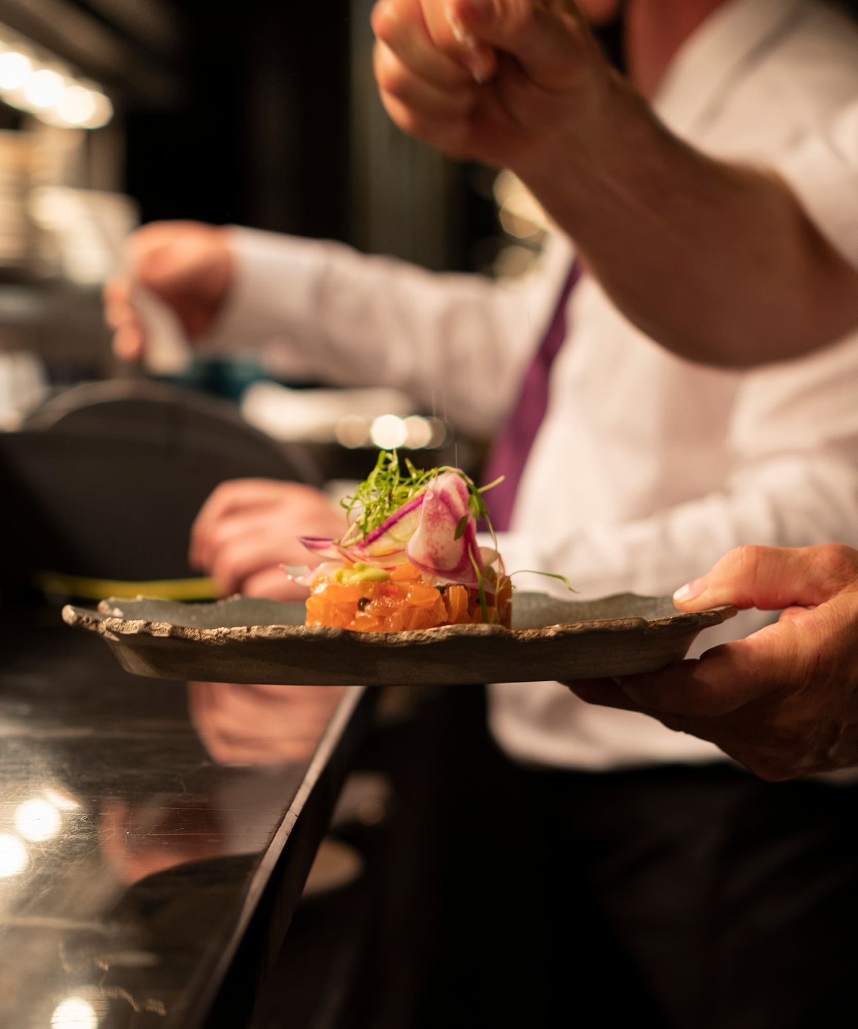 Fine dining chef presenting beautifully plated salmon tartare in a restaurant.