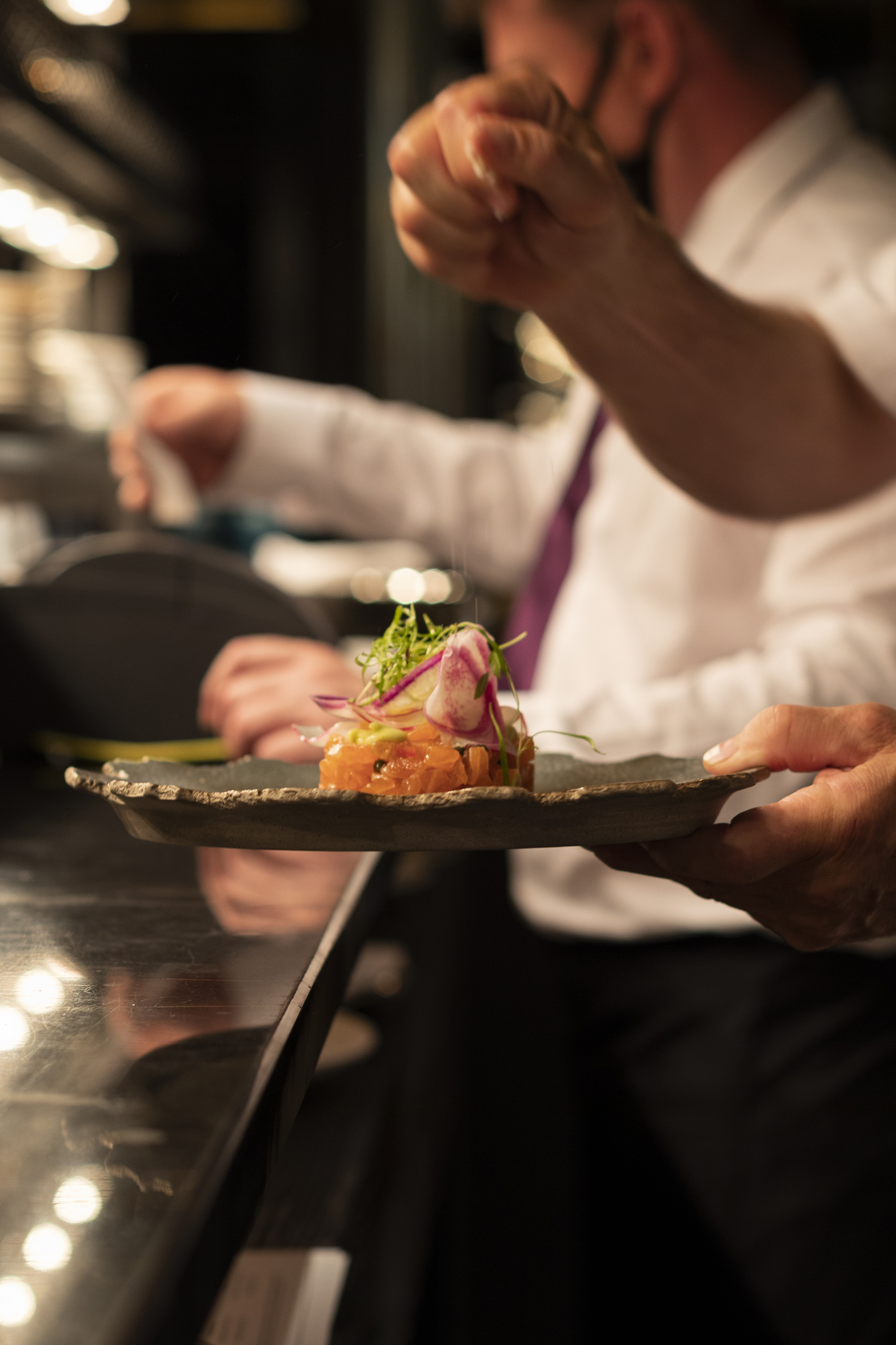 Fine dining chef presenting beautifully plated salmon tartare in a restaurant.