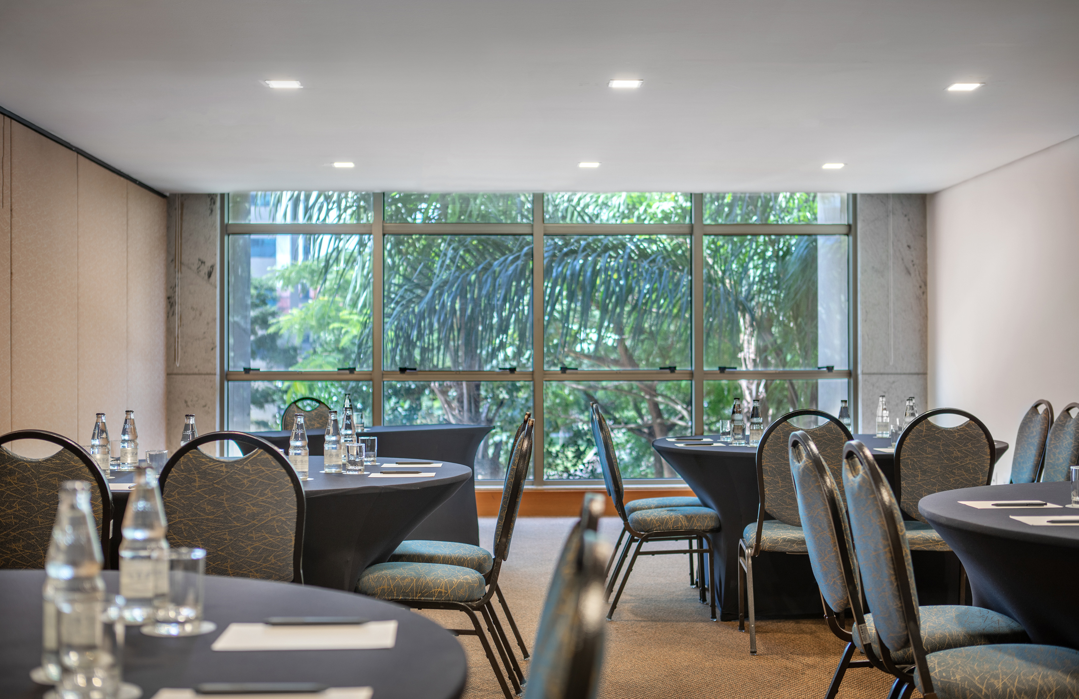 Conference room with round tables, chairs, and large window overlooking trees.