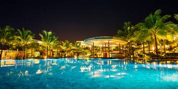 a pool with palm trees and a building at night