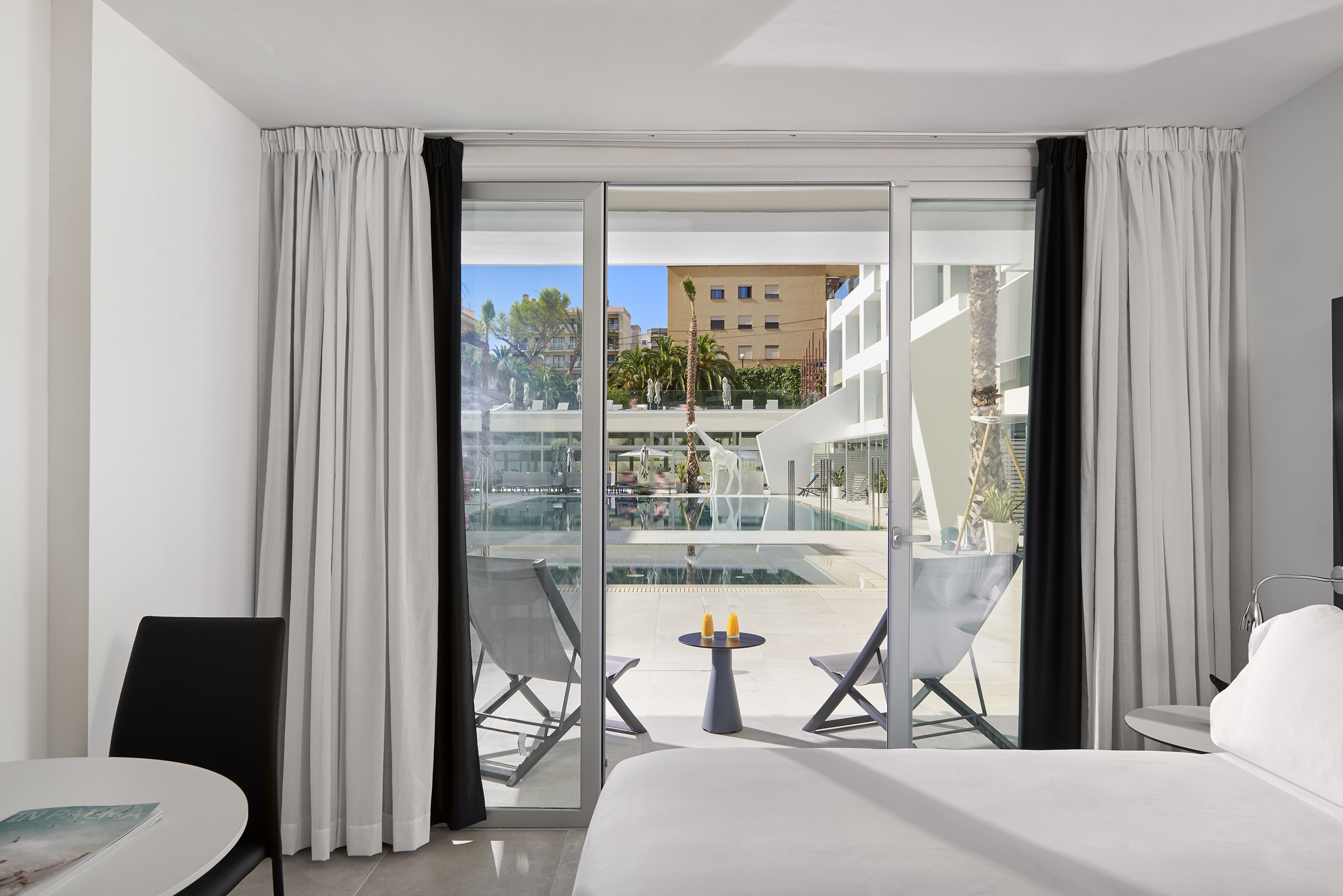 Modern hotel room with balcony, pool view, lounge chairs, and orange juice.