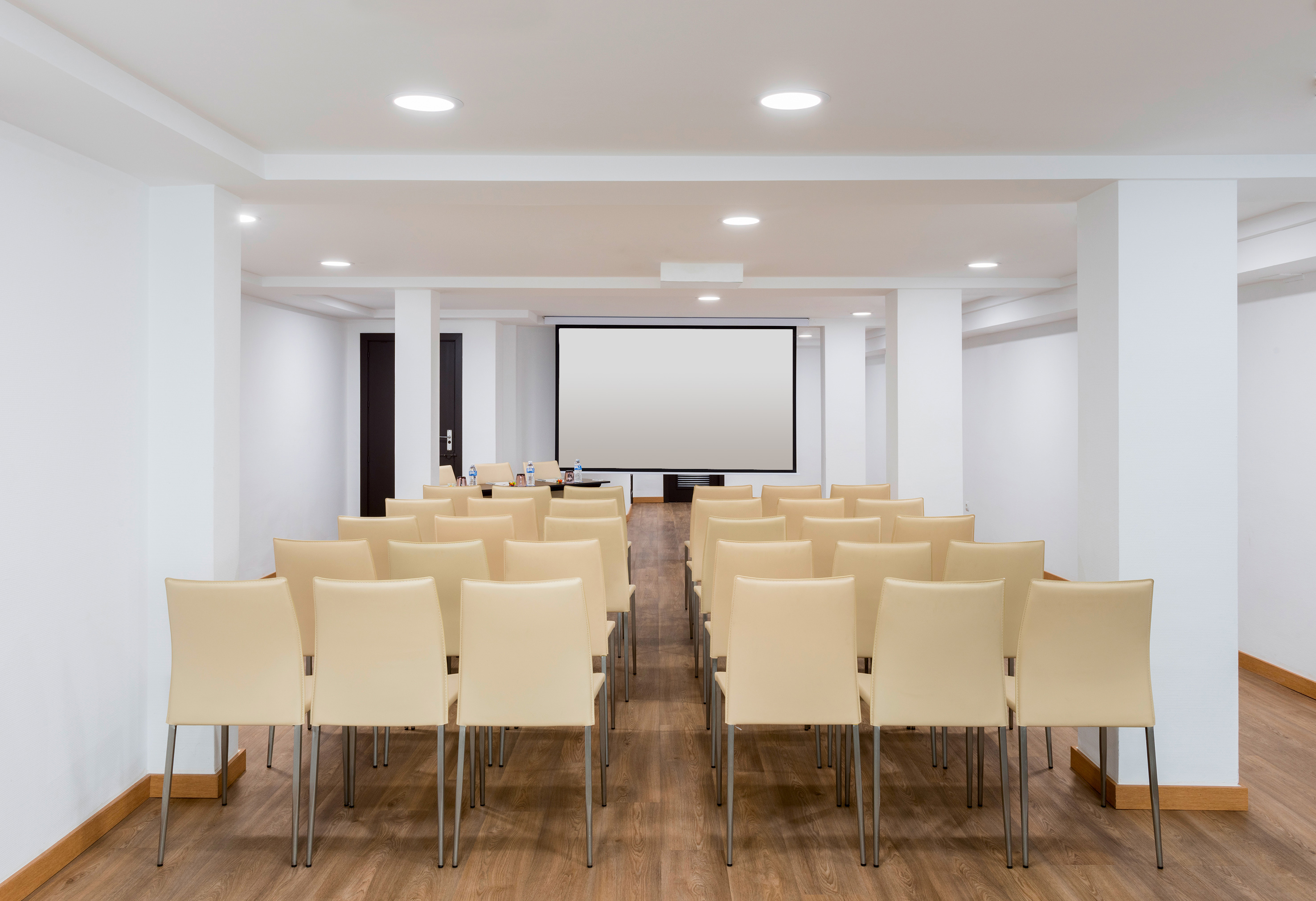 Empty conference room with rows of chairs, projector screen, and wood floor. - Santa Bárbara - Hotel Alicante Gran Sol Affiliated by Meliá, 阿利坎特