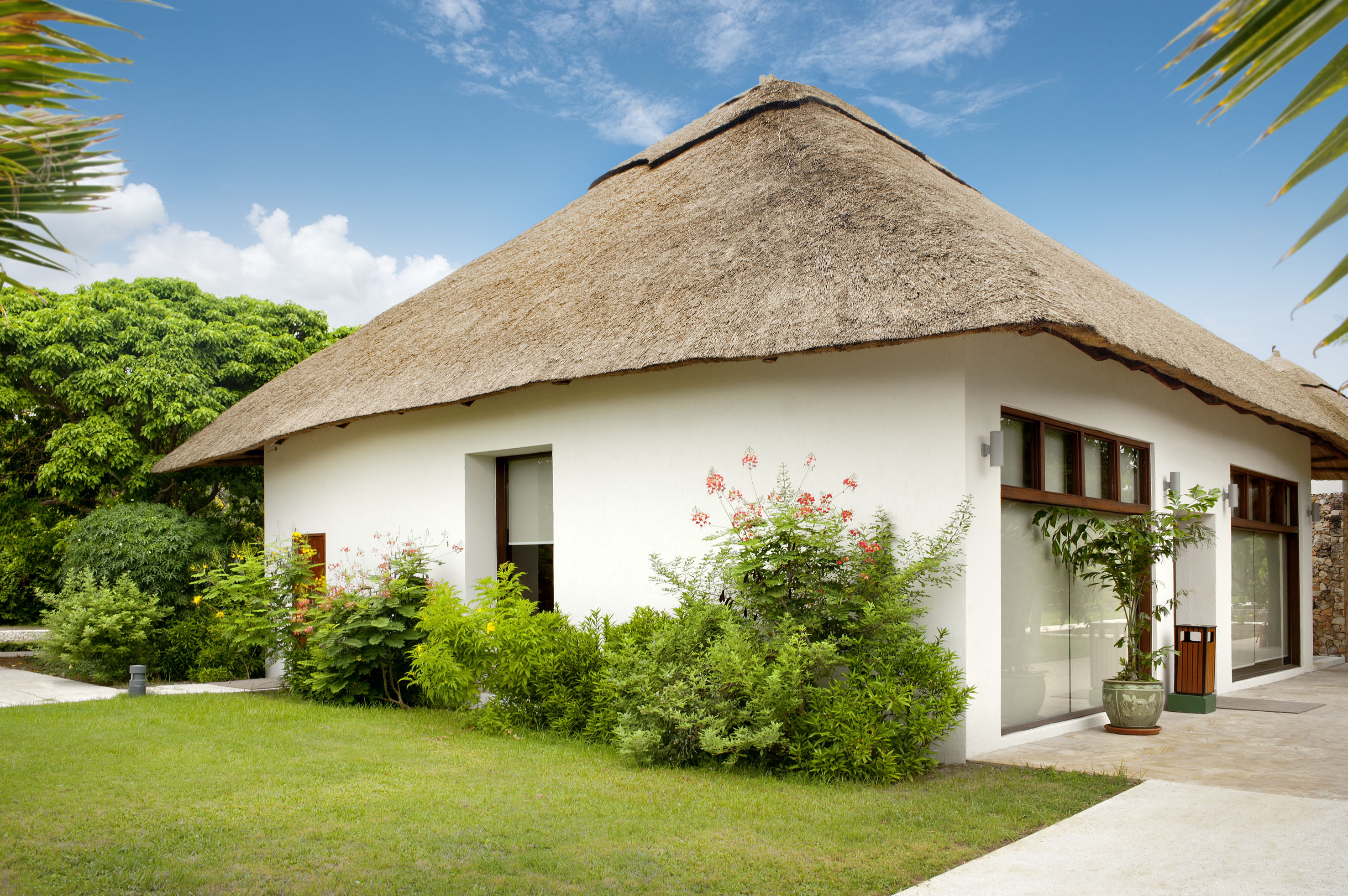 Modern white tropical house with a thatched roof and lush green garden.