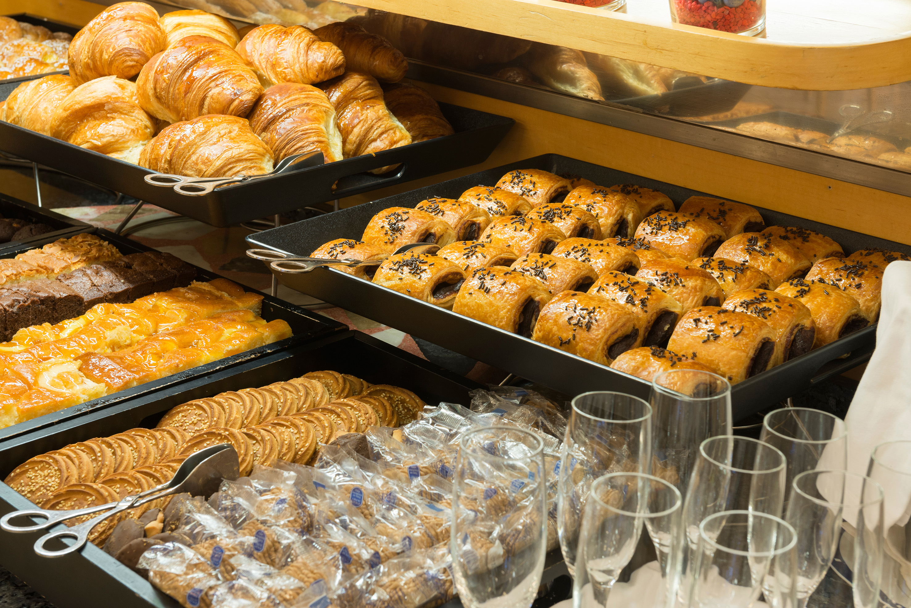 Breakfast buffet with golden croissants, chocolate pastries, cakes, and wrapped cookies.