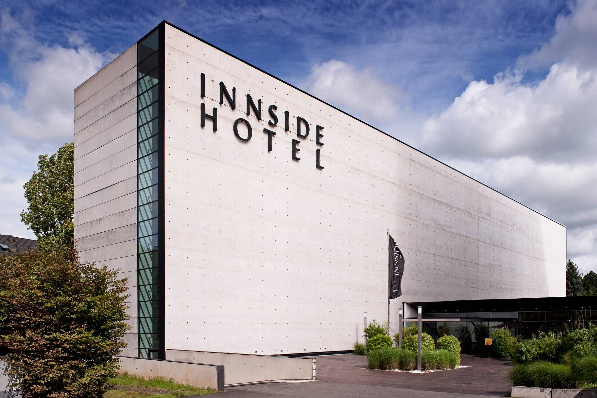 INNSIDE Hotel modern concrete building exterior, glass facade, blue sky.