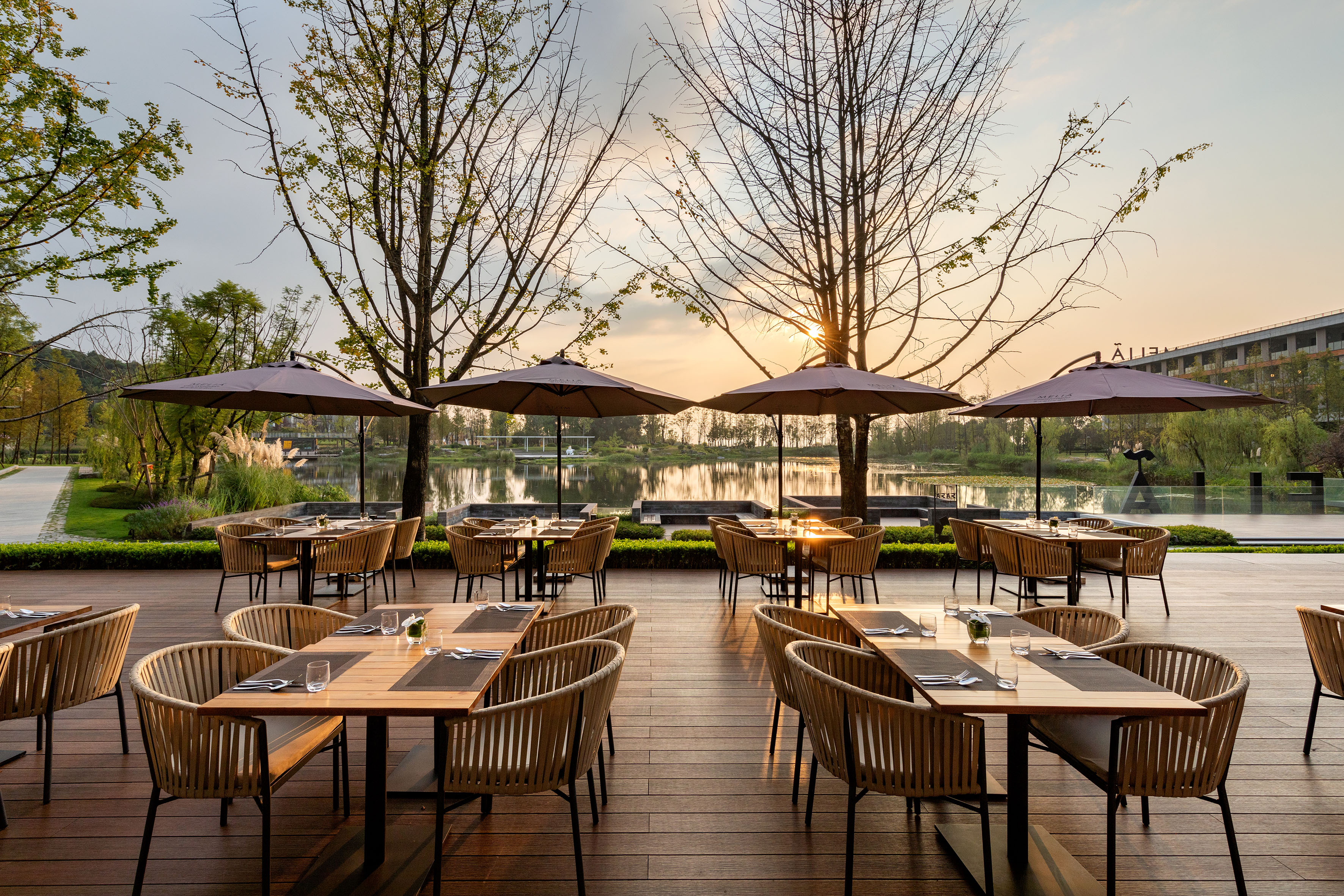 Lakeside outdoor dining patio at sunset, with dining tables and umbrellas.