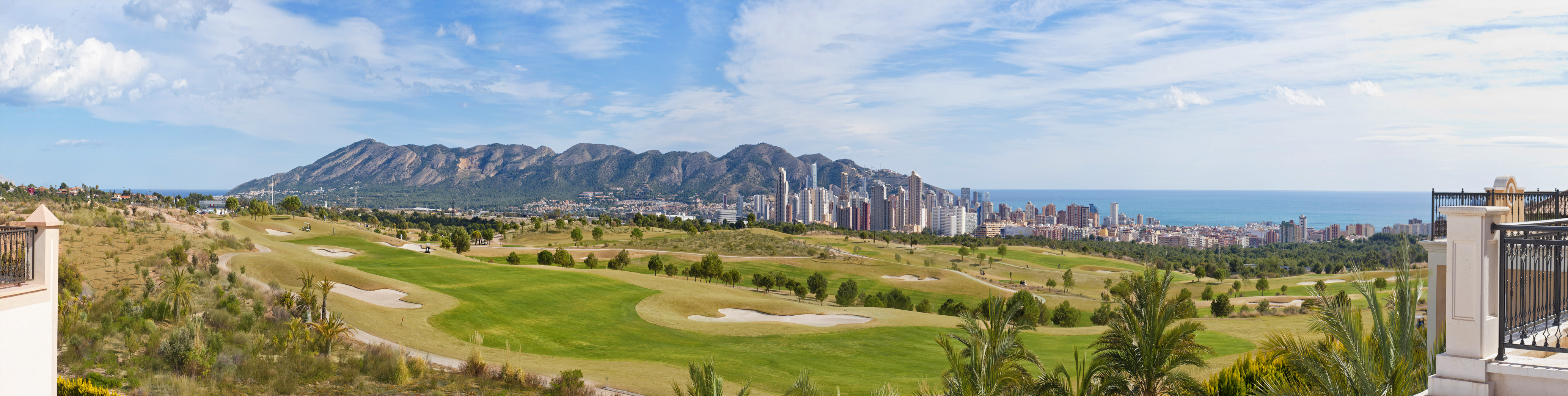 Panoramic golf resort with Benidorm city skyline, mountains, and Mediterranean coast.