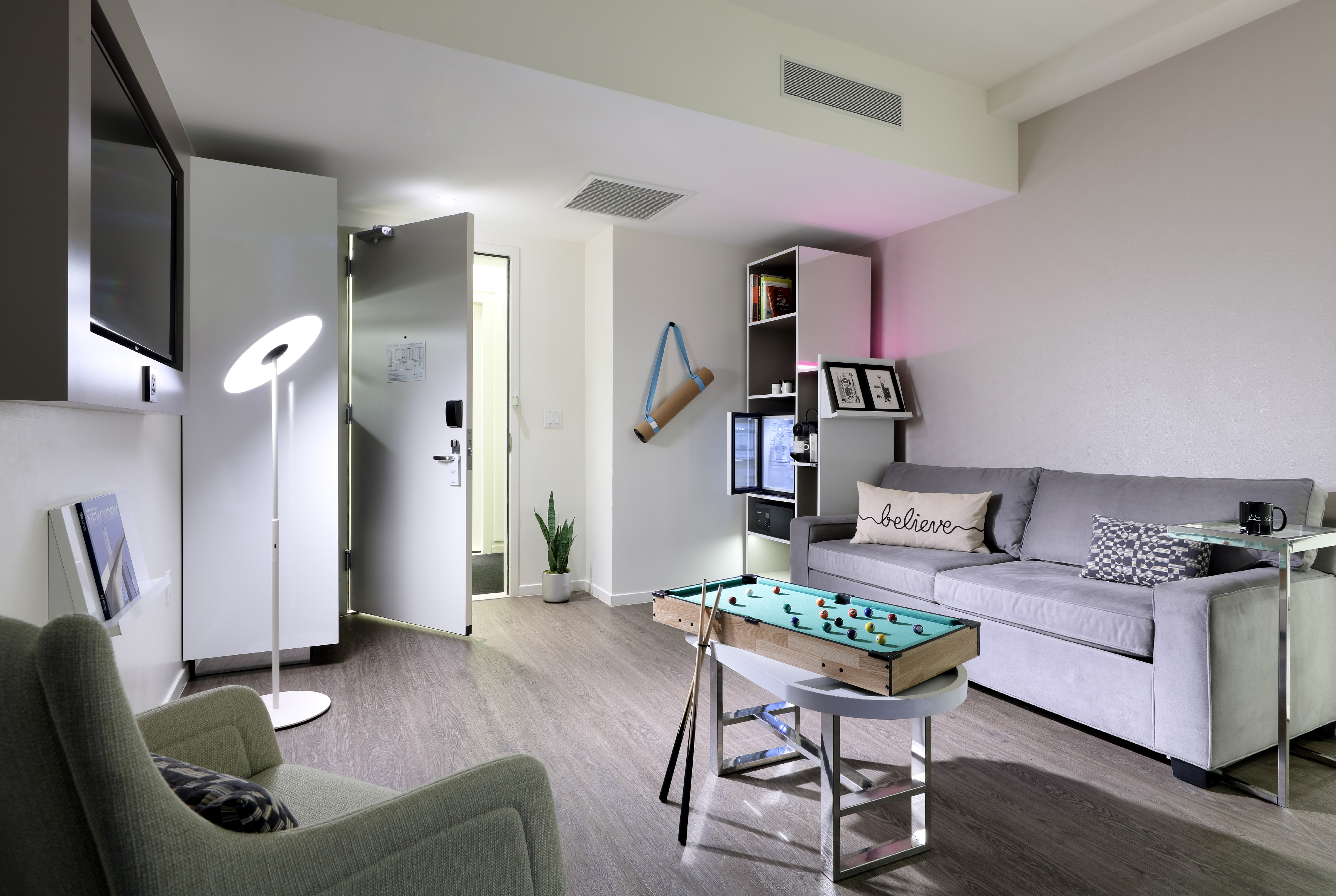 Contemporary hotel suite living room with grey sofa, mini pool table, TV.