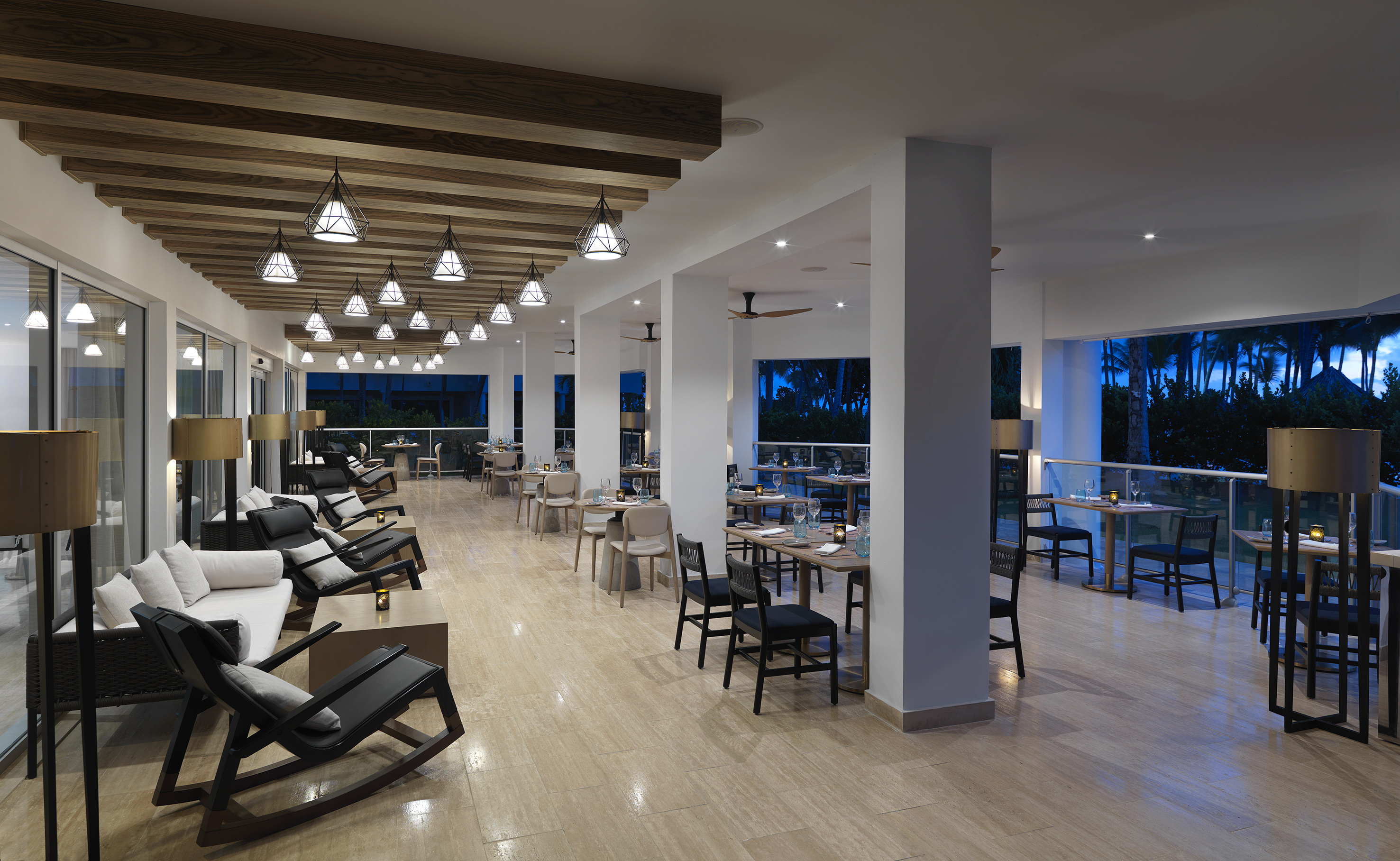 Modern restaurant with diverse seating, stylish lighting, and evening tropical view.