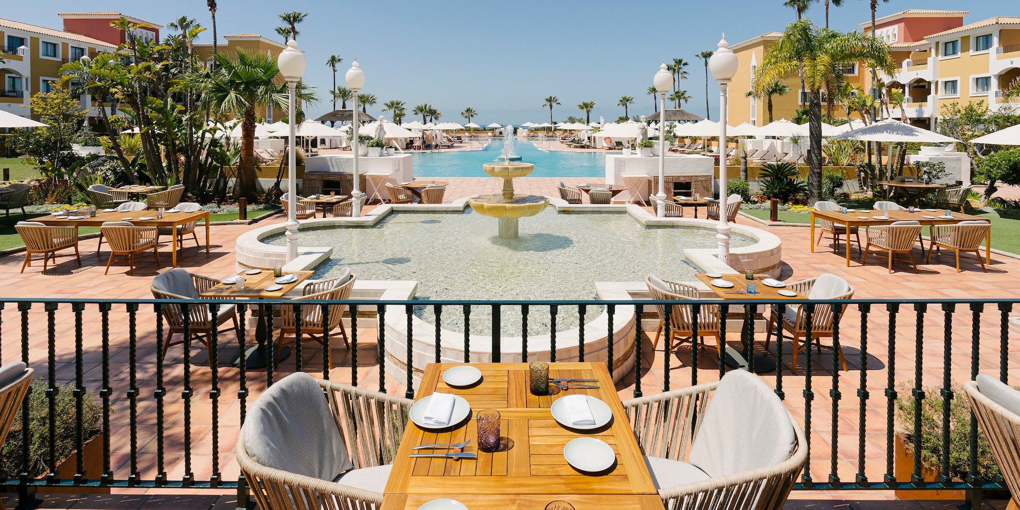 a table and chairs outside with a fountain and palm trees