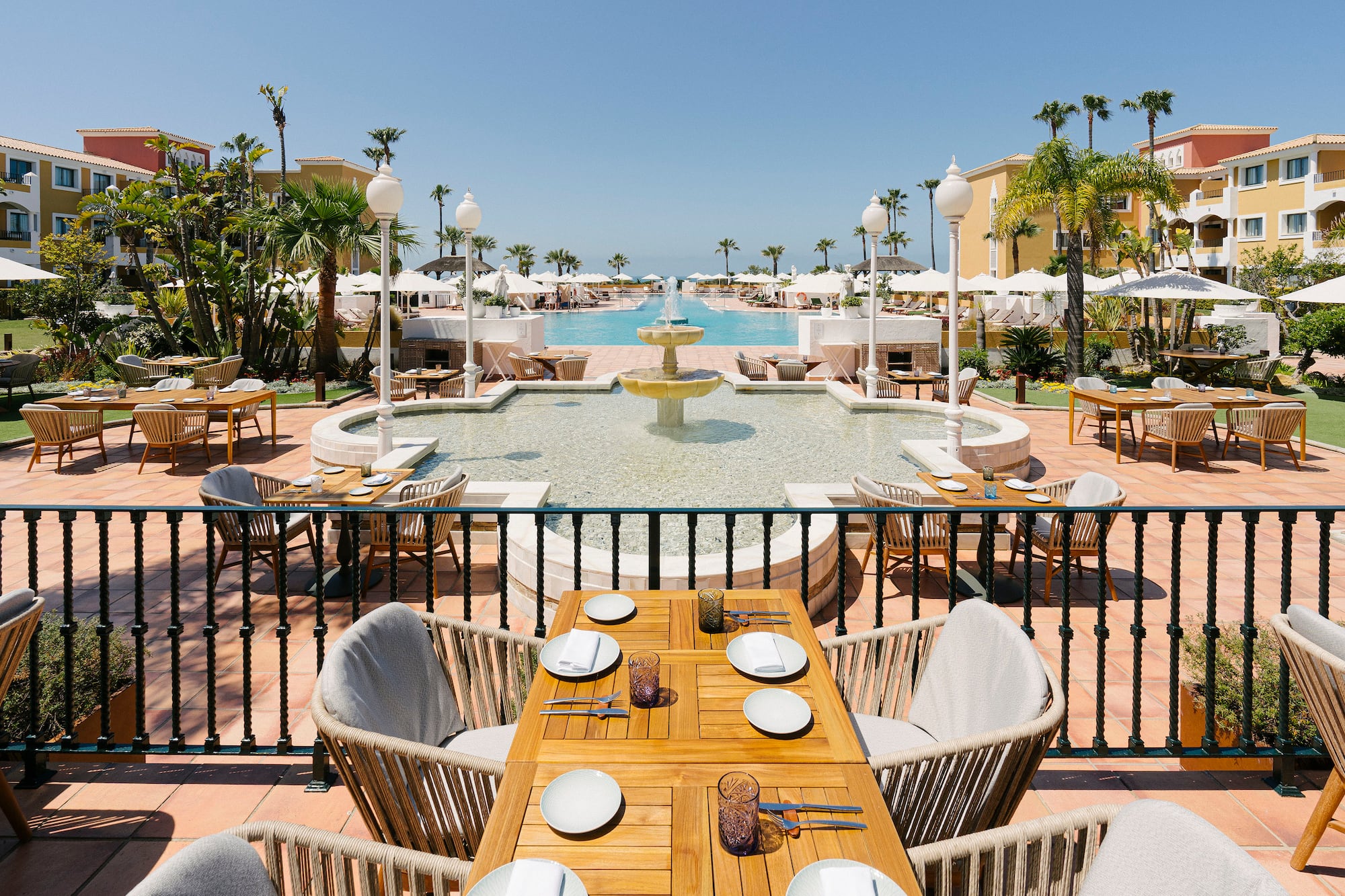 a table and chairs outside with a fountain and palm trees
