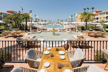 a table and chairs outside with a fountain and palm trees