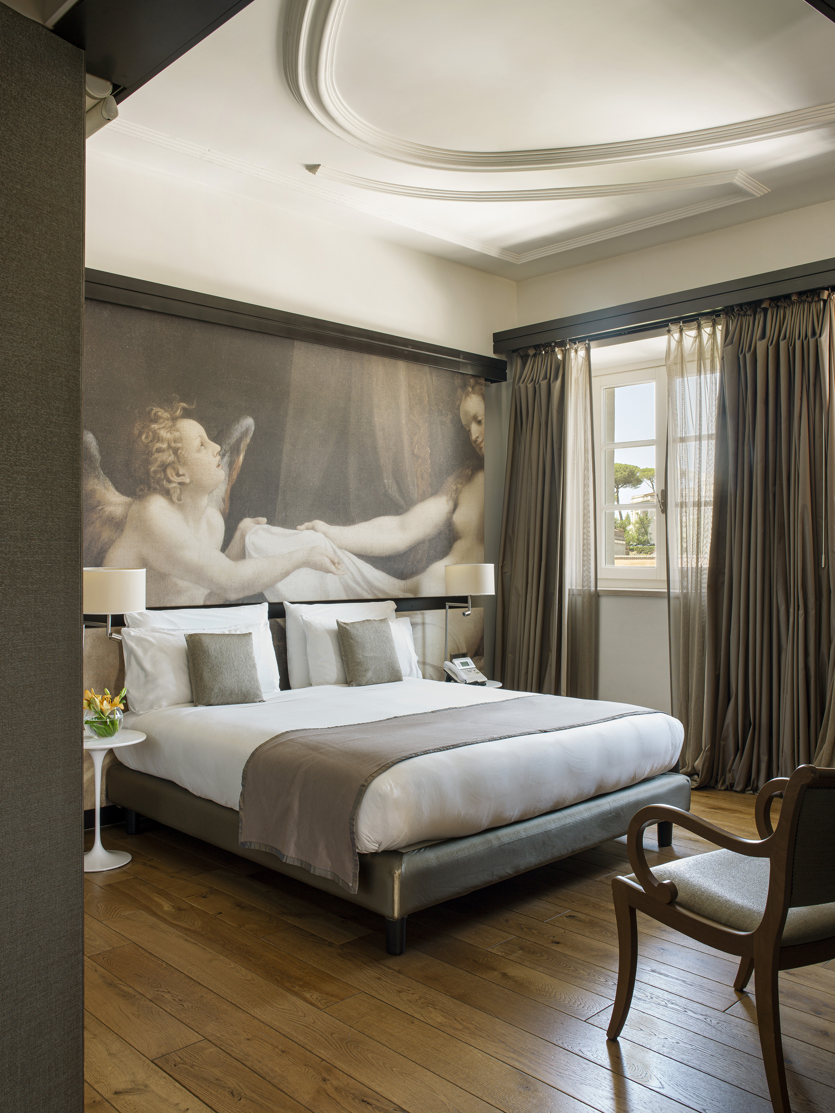 Luxury hotel bedroom with classical angel mural, king bed, and dark curtains.