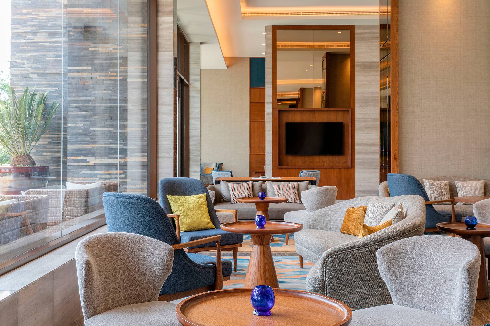 Luxury hotel lounge with stylish armchairs, wood tables, and a large window view.