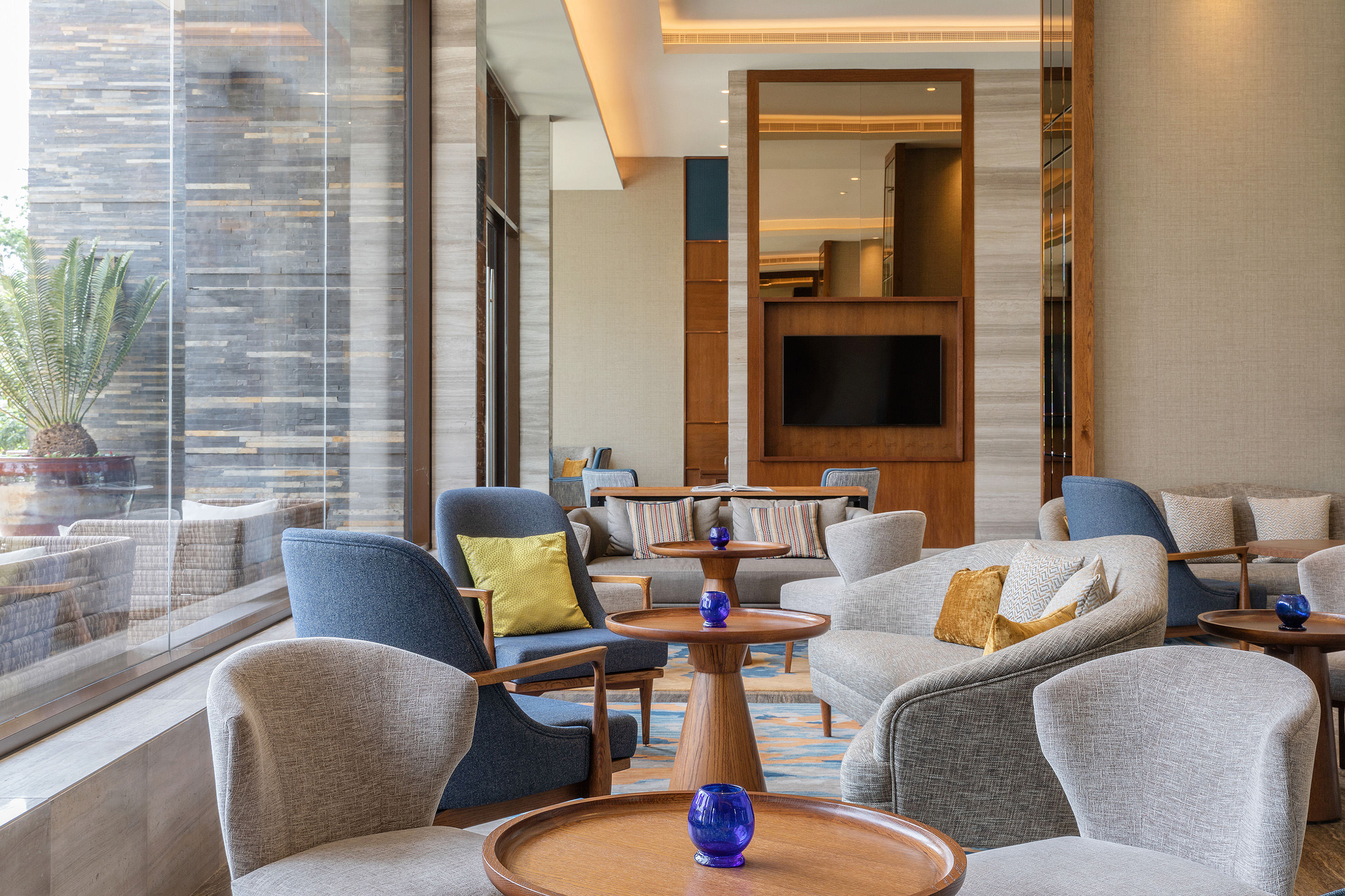 Luxury hotel lounge with stylish armchairs, wood tables, and a large window view.