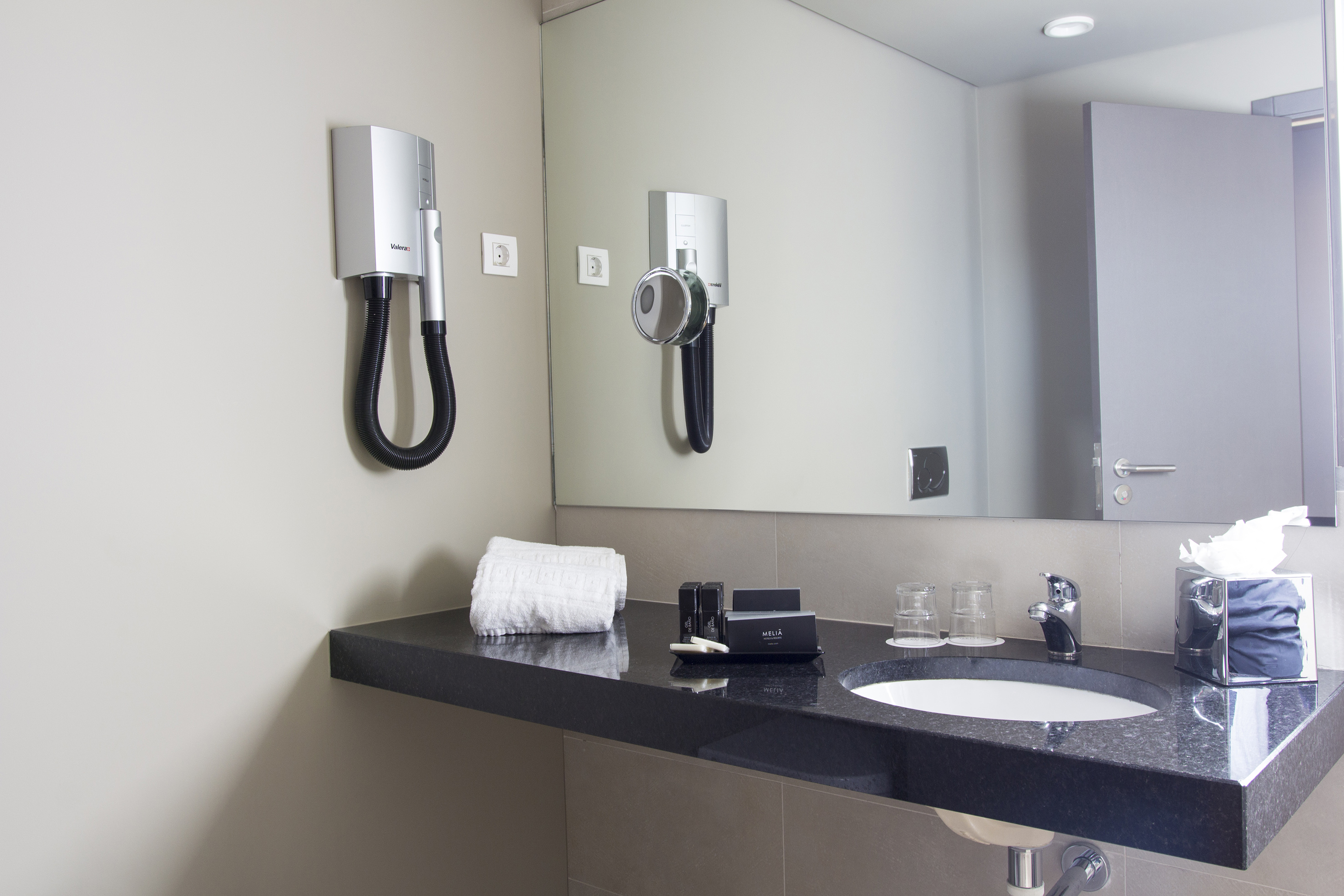 Hotel bathroom vanity with dark granite counter, sink, hairdryer, and amenities.