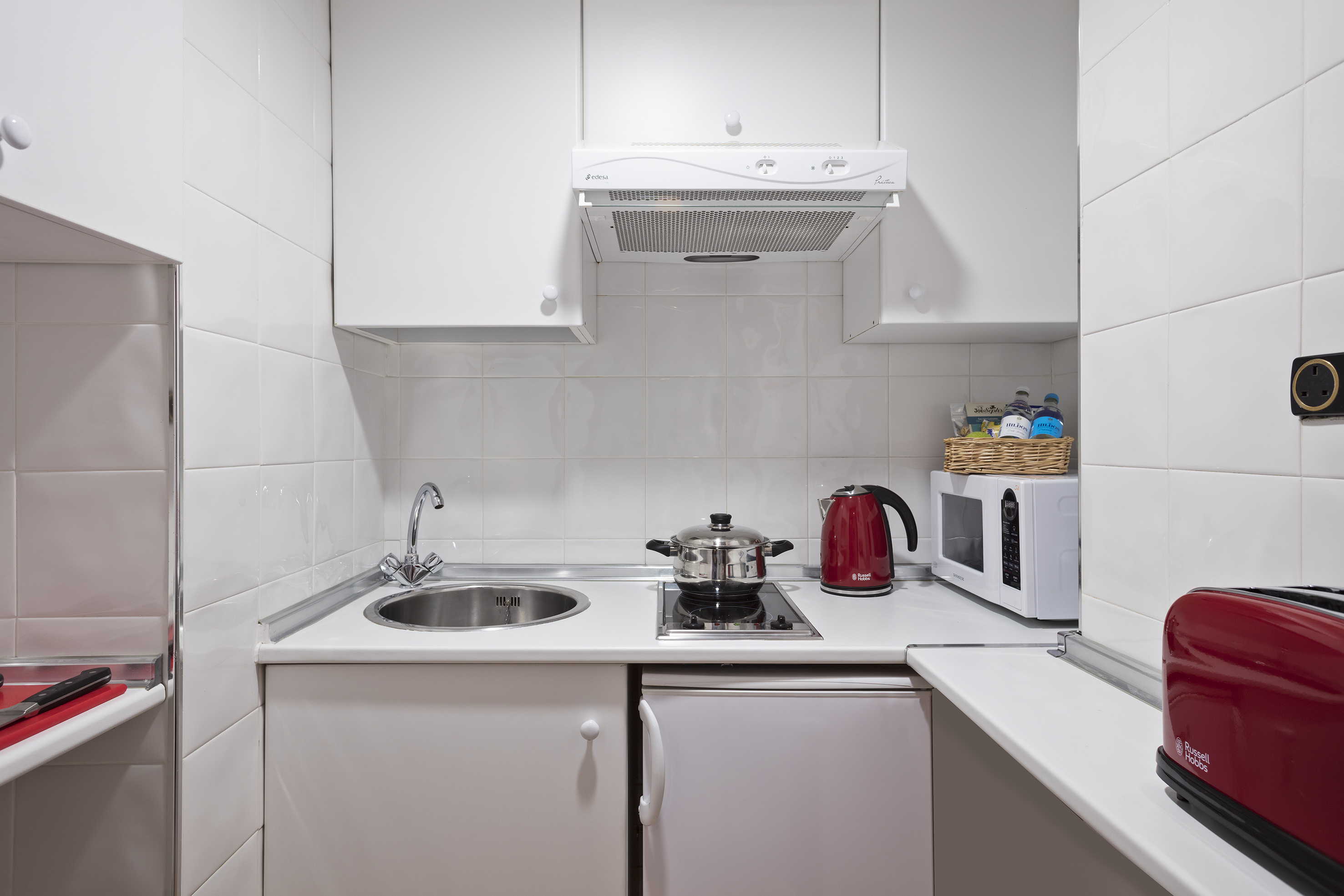 Modern white kitchenette with sink, built-in hob, microwave, and red appliances.