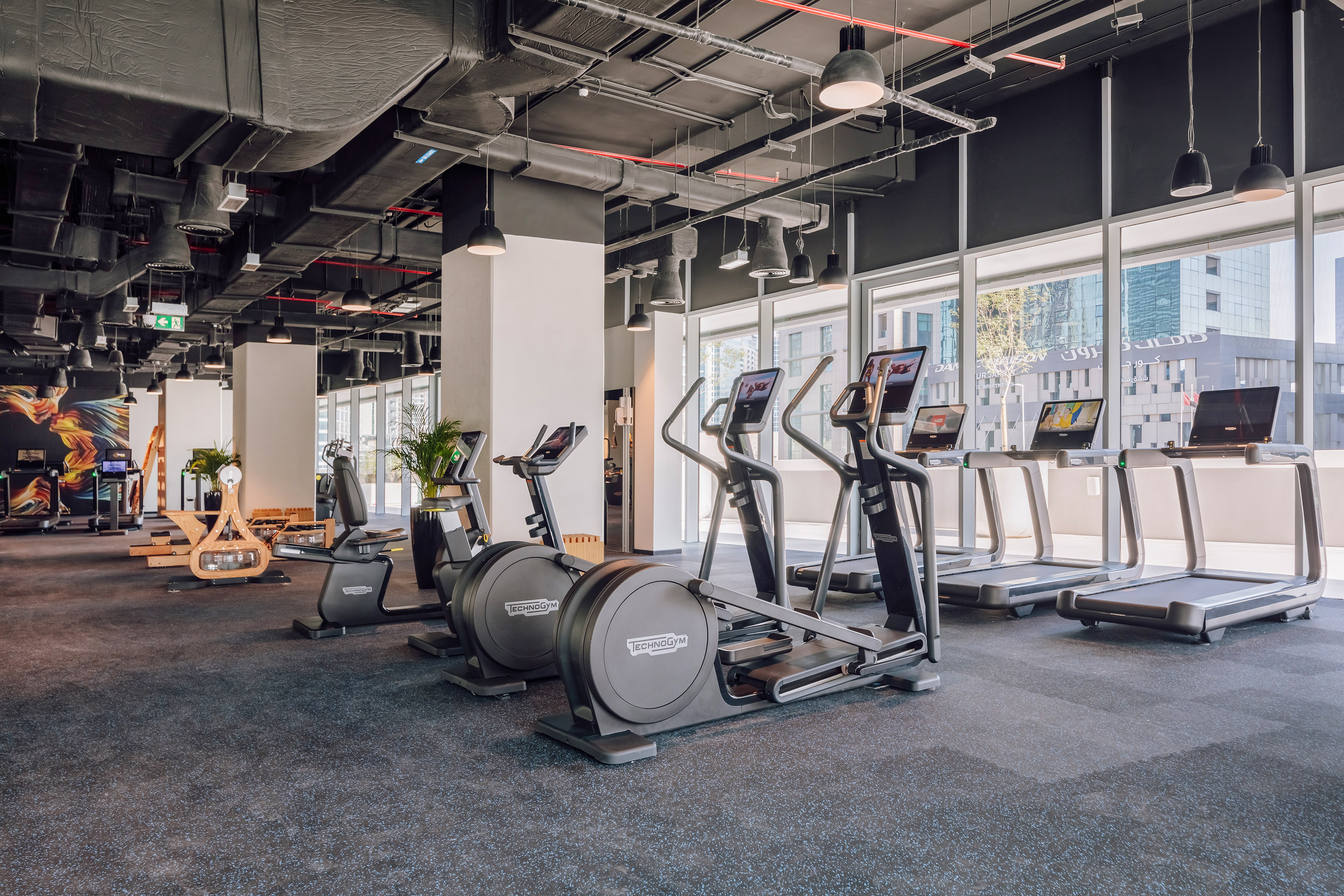Technogym ellipticals, treadmills, bikes in a modern gym with large windows.