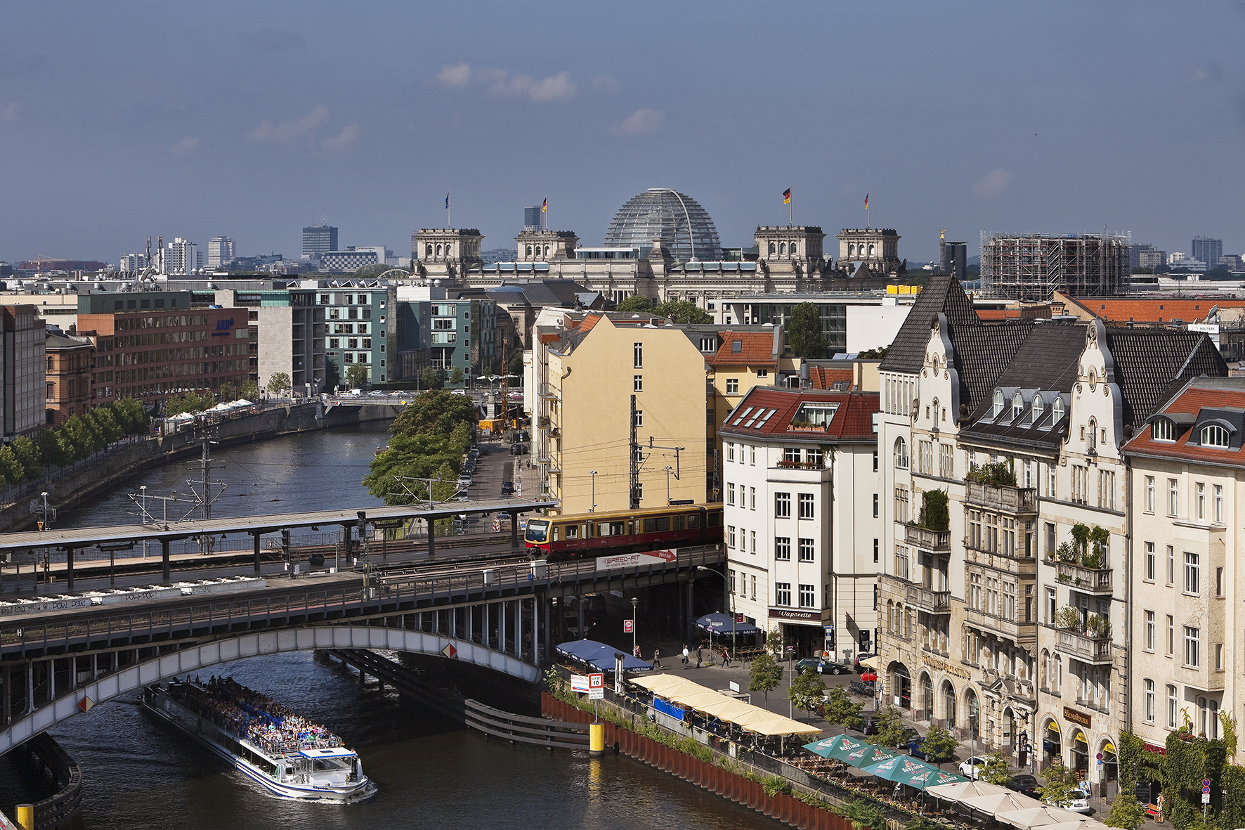 Berlin cityscape: Spree River, Reichstag, train on bridge, and tour boat.