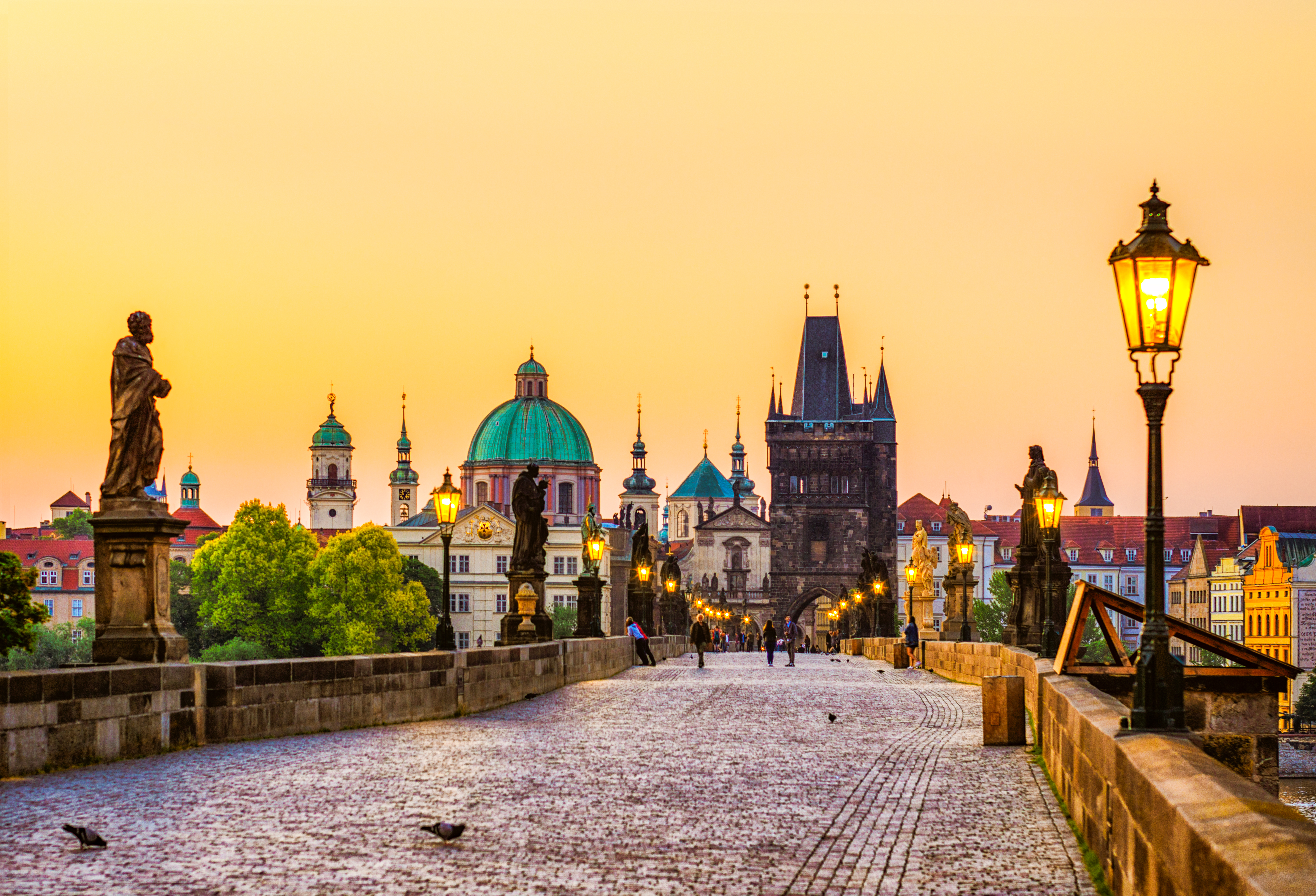 Golden hour view of Prague's Charles Bridge with statues and historic towers.