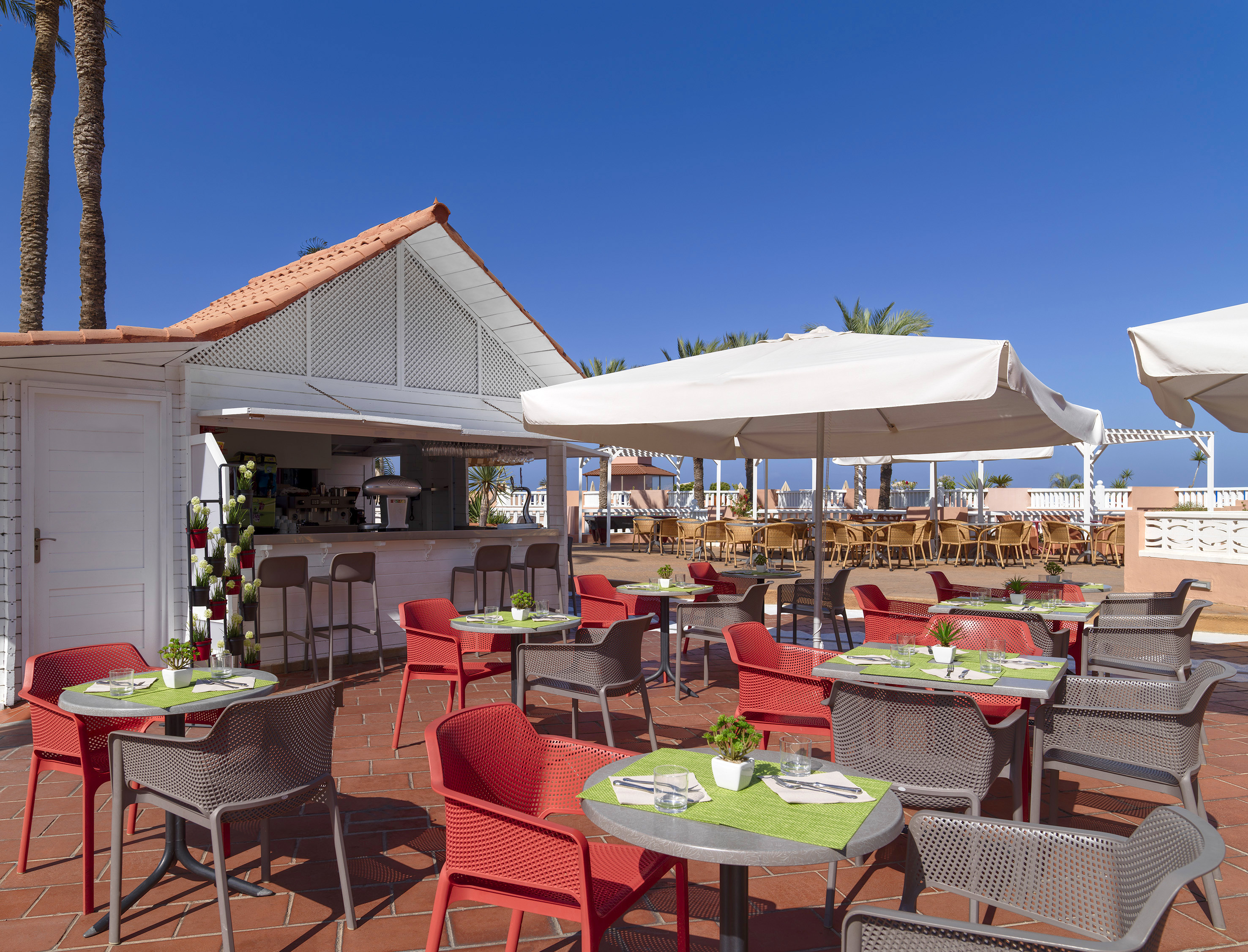 Resort outdoor patio restaurant and bar with red chairs, white umbrellas.