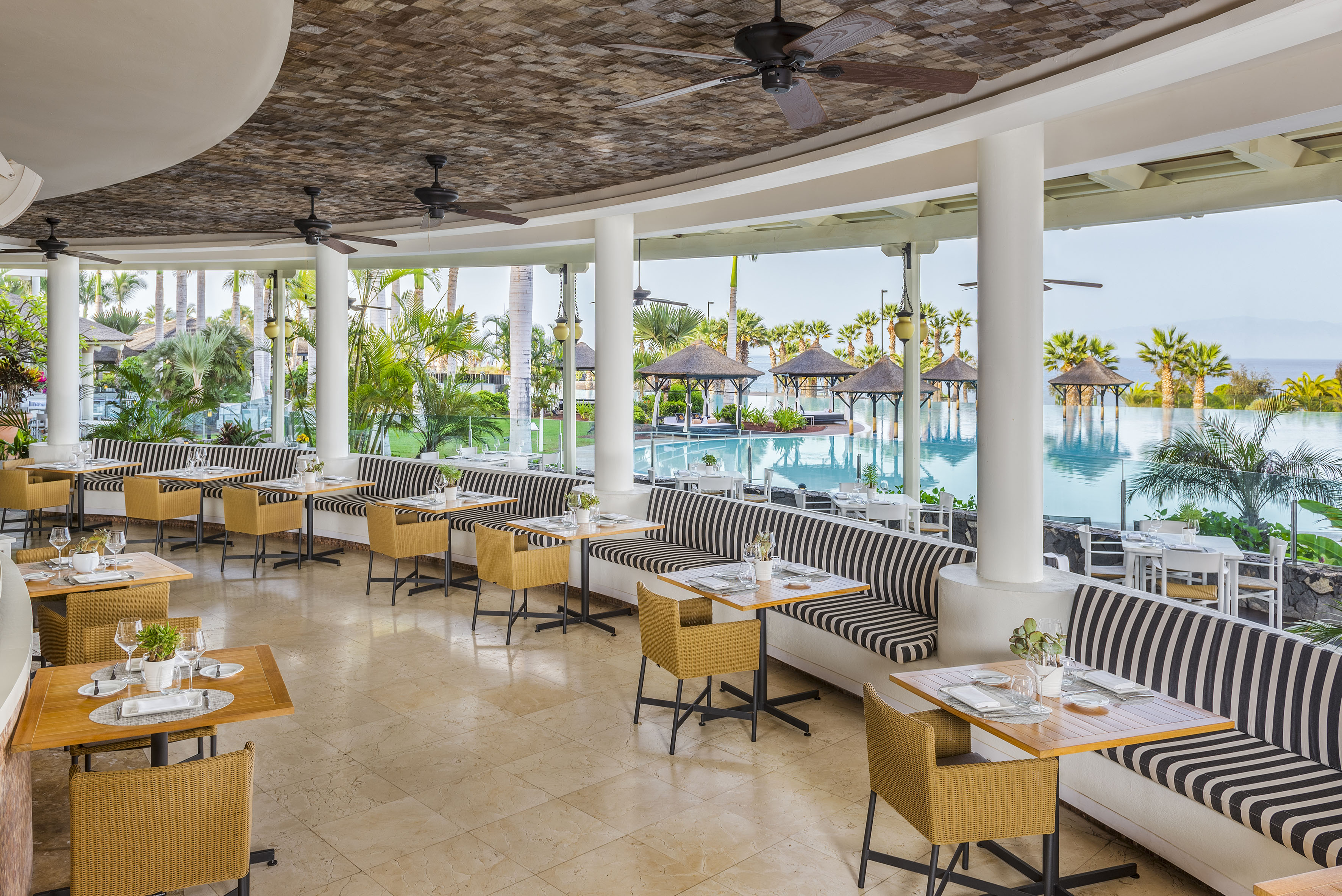 Resort restaurant with pool view, outdoor dining, striped banquette seating.