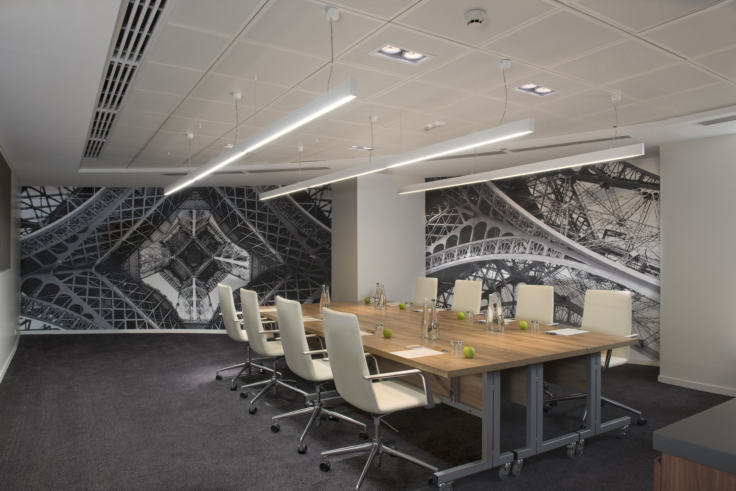 Modern conference room with Eiffel Tower mural, long wooden table, white chairs.