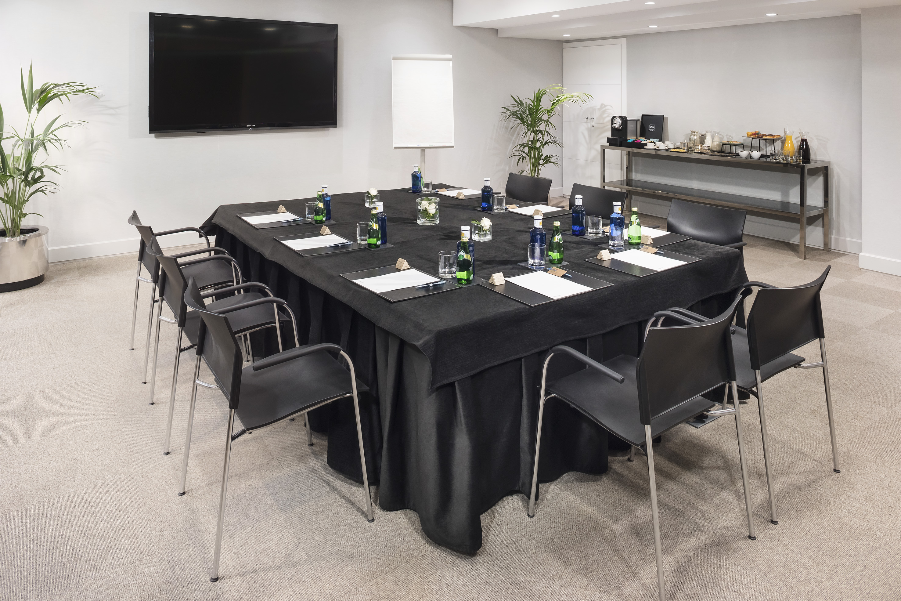 Contemporary meeting room with square conference table, screen, and refreshments.