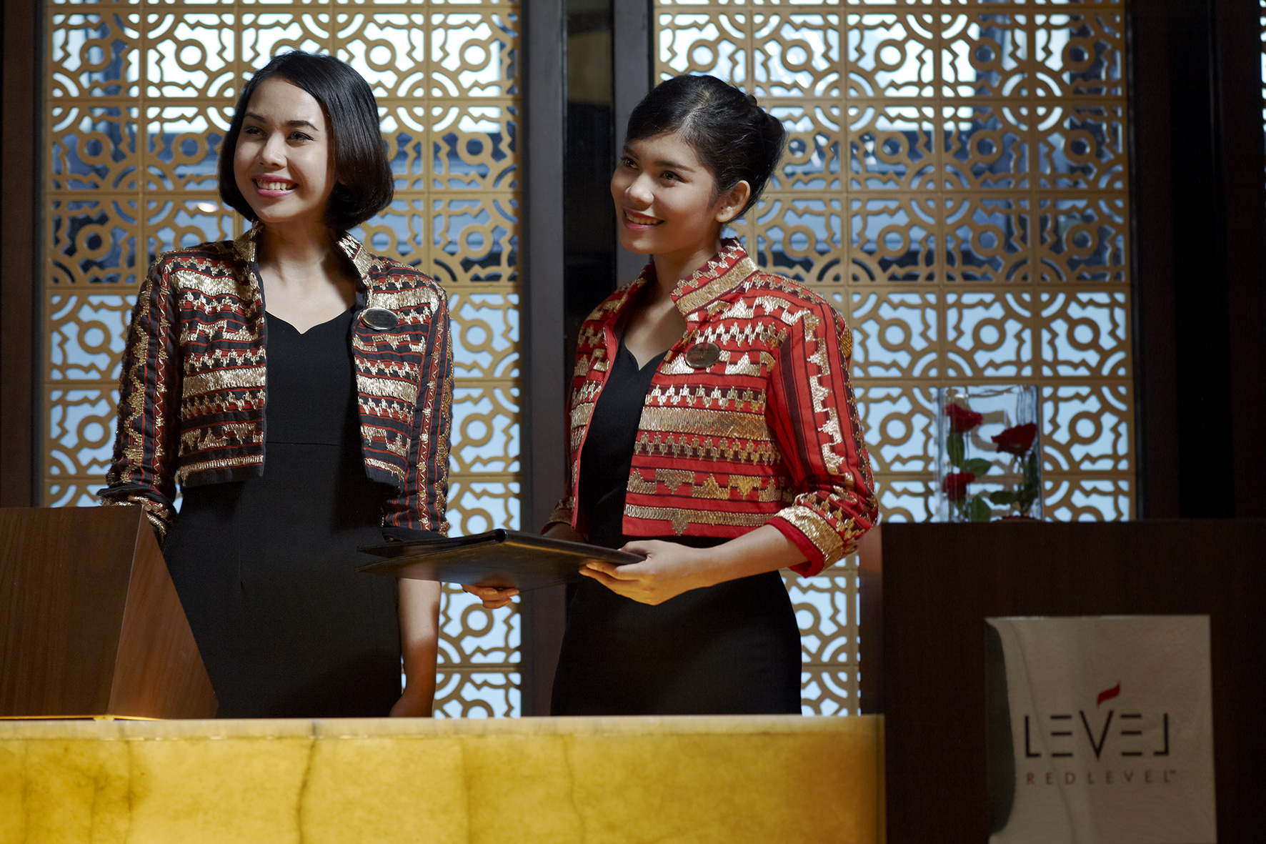 Smiling LEVEL REDLEVEL hotel receptionists in uniform at front desk.