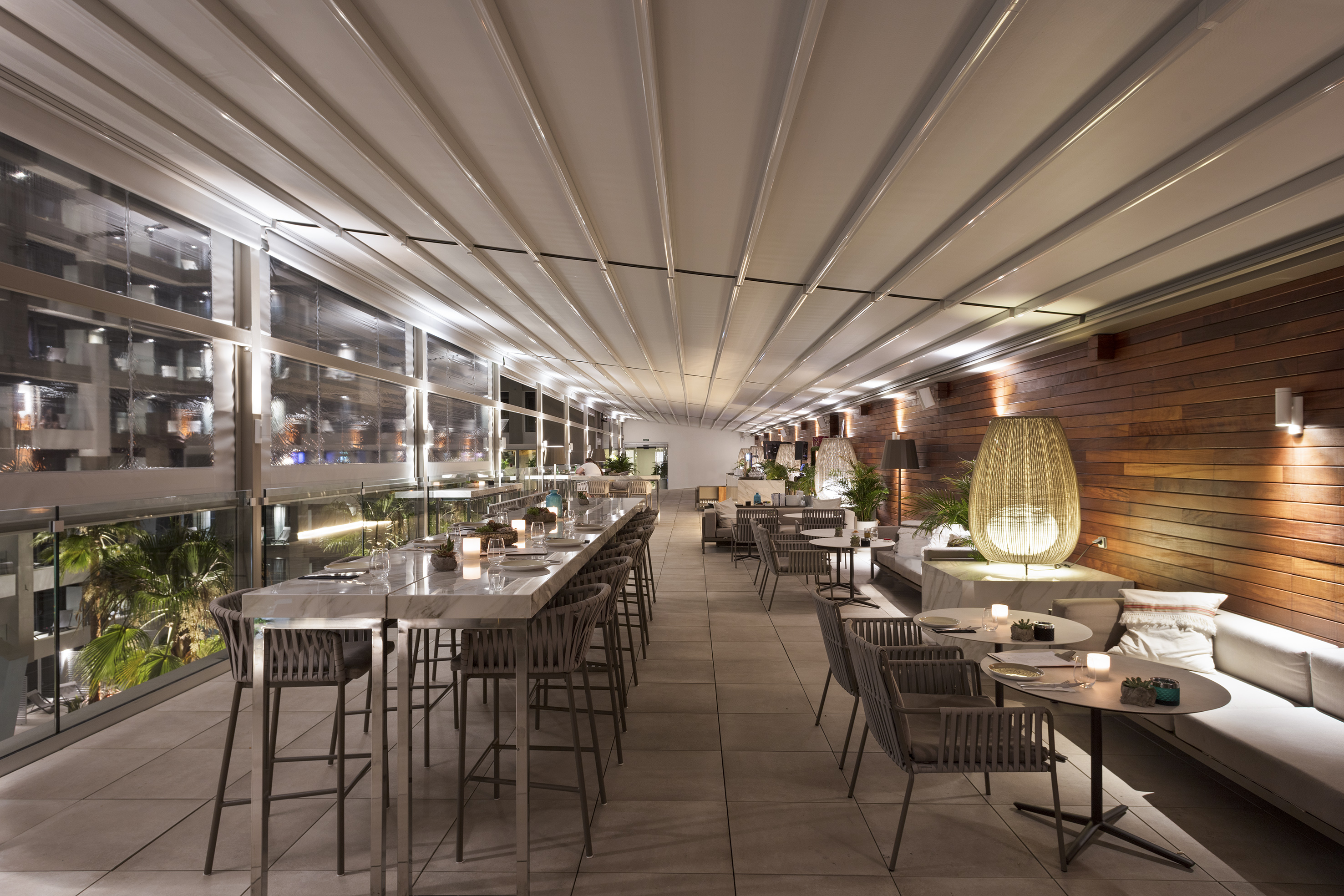 Modern terrace restaurant with retractable roof system and night city view.