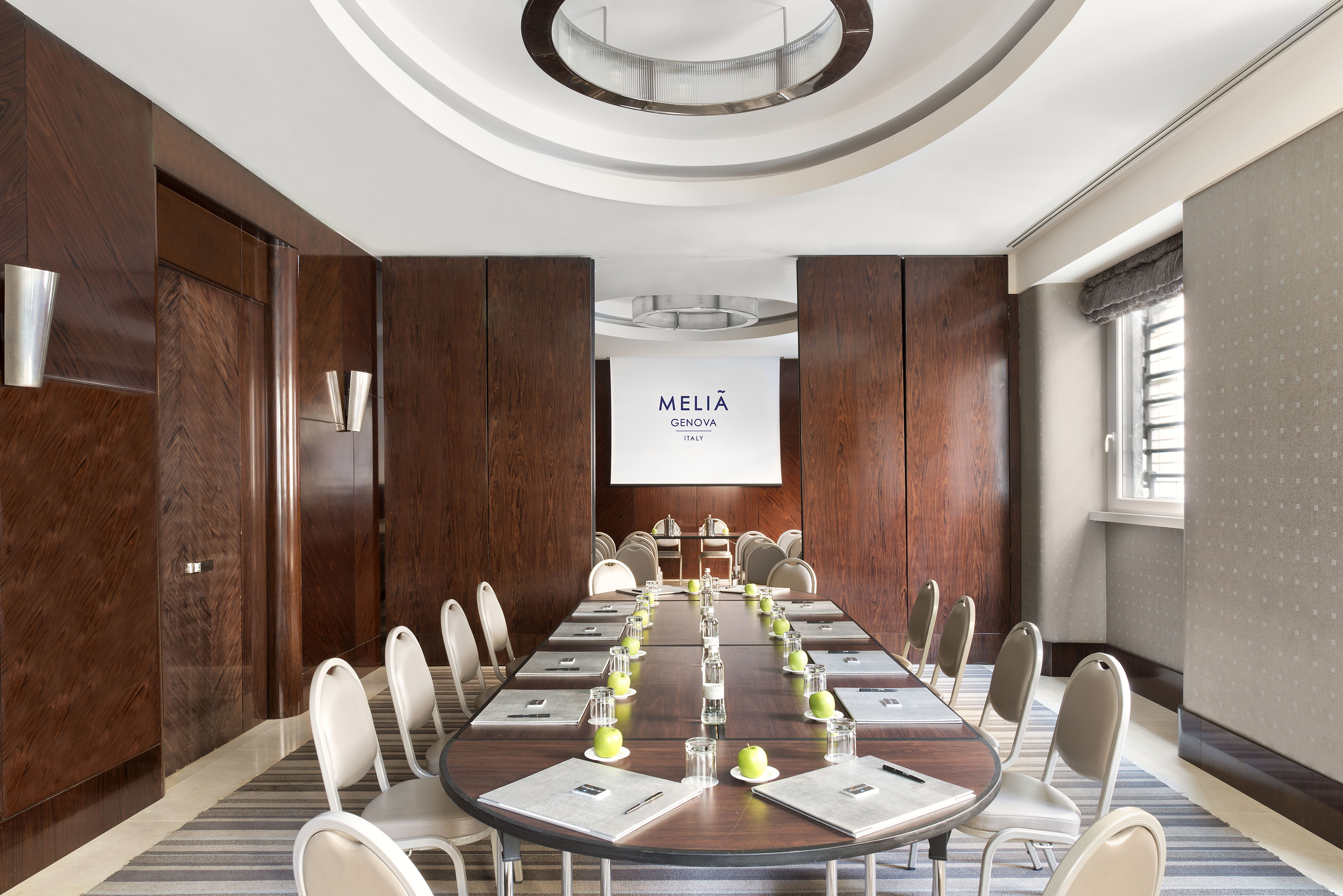 Meliá Genova boardroom setup with long table, chairs, and projector.